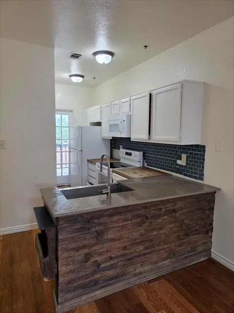 Kitchen featuring a wood-finish island with integrated sink, white cabinetry, a dark subway tile backsplash, and wood-finish flooring