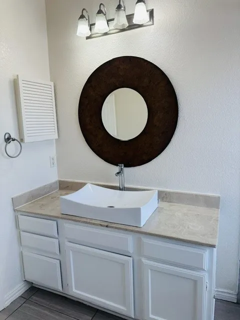 White vanity with shaker style cabinetry, countertop, and a vessel sink