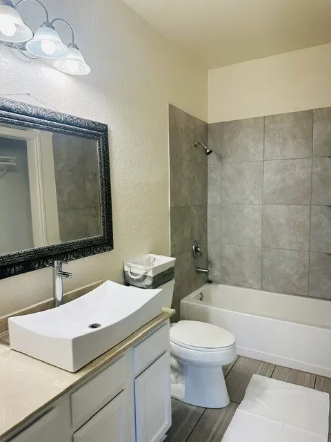 Bathroom featuring a rectangular vessel sink, light-toned countertop, white cabinetry, and a full-size bathtub with gray tile surround