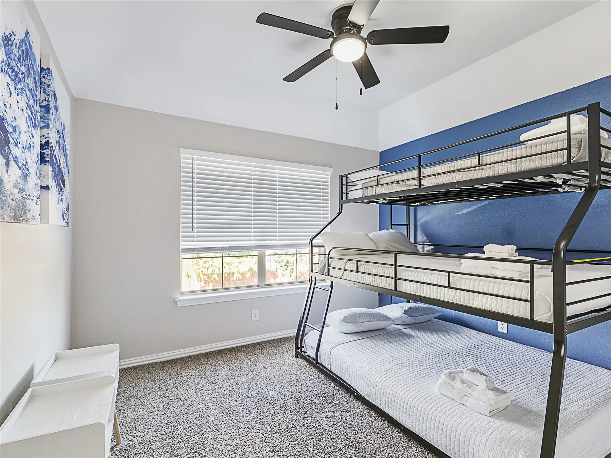 Bedroom featuring a black metal bunk bed, light gray walls with a blue accent wall, a window with horizontal blinds, and a ceiling fan with integrated lighting