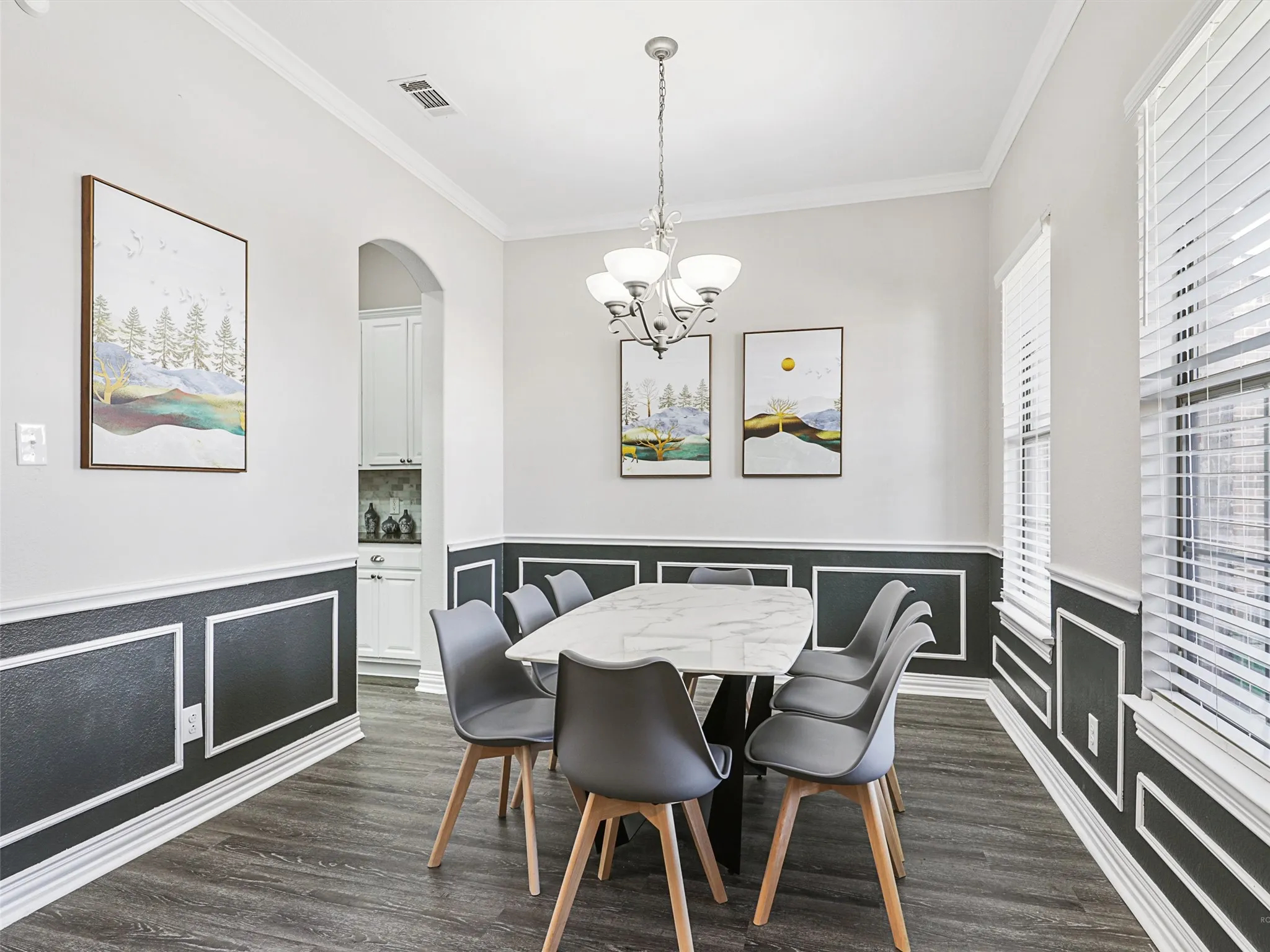 Dining area featuring dark wood-finish flooring, wainscoting with decorative trim, and a white crown molding ceiling