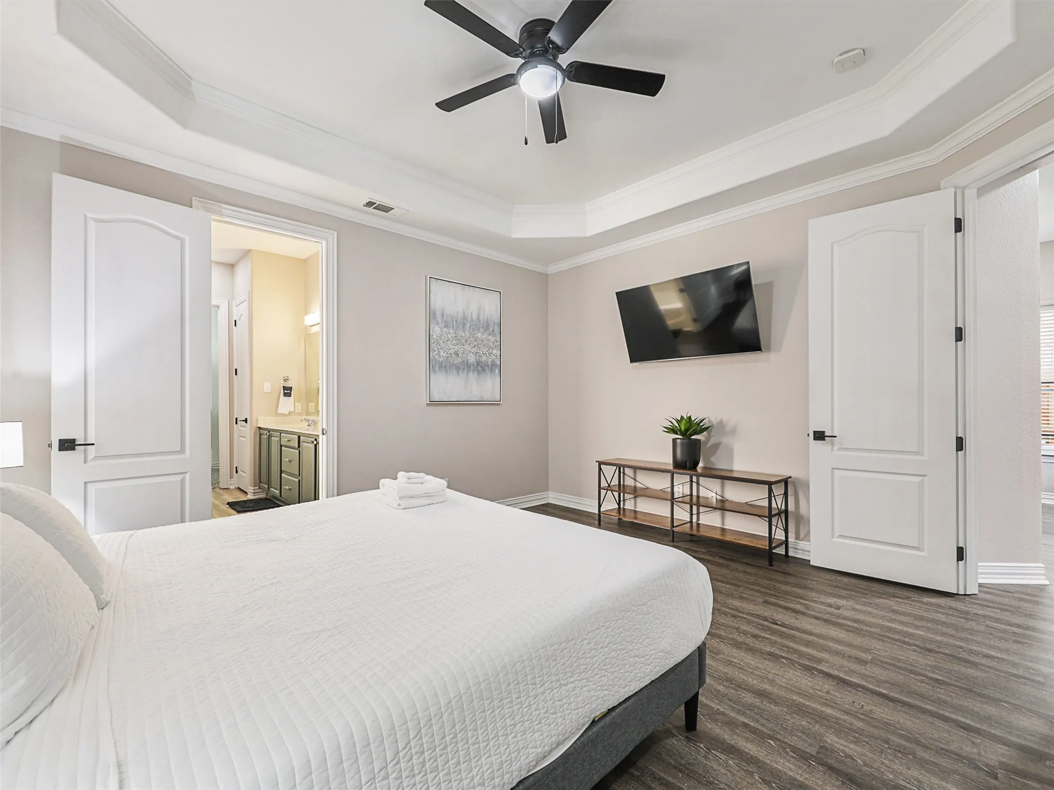 Bedroom featuring wood-finish flooring, a tray ceiling with a ceiling fan, and two panel doors