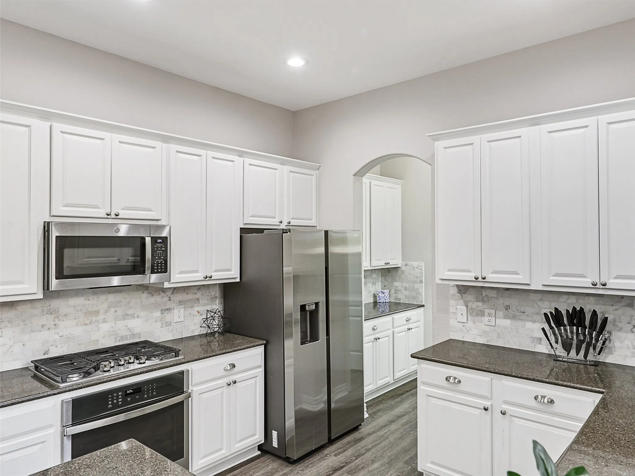 Modern kitchen featuring extensive white cabinetry, dark granite-style countertops, and a stone-tiled backsplash