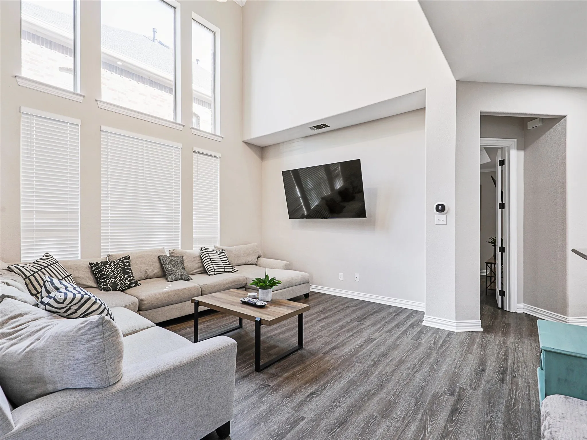Great room featuring a vaulted ceiling, wood-finish flooring, tall windows with blinds, and white baseboards