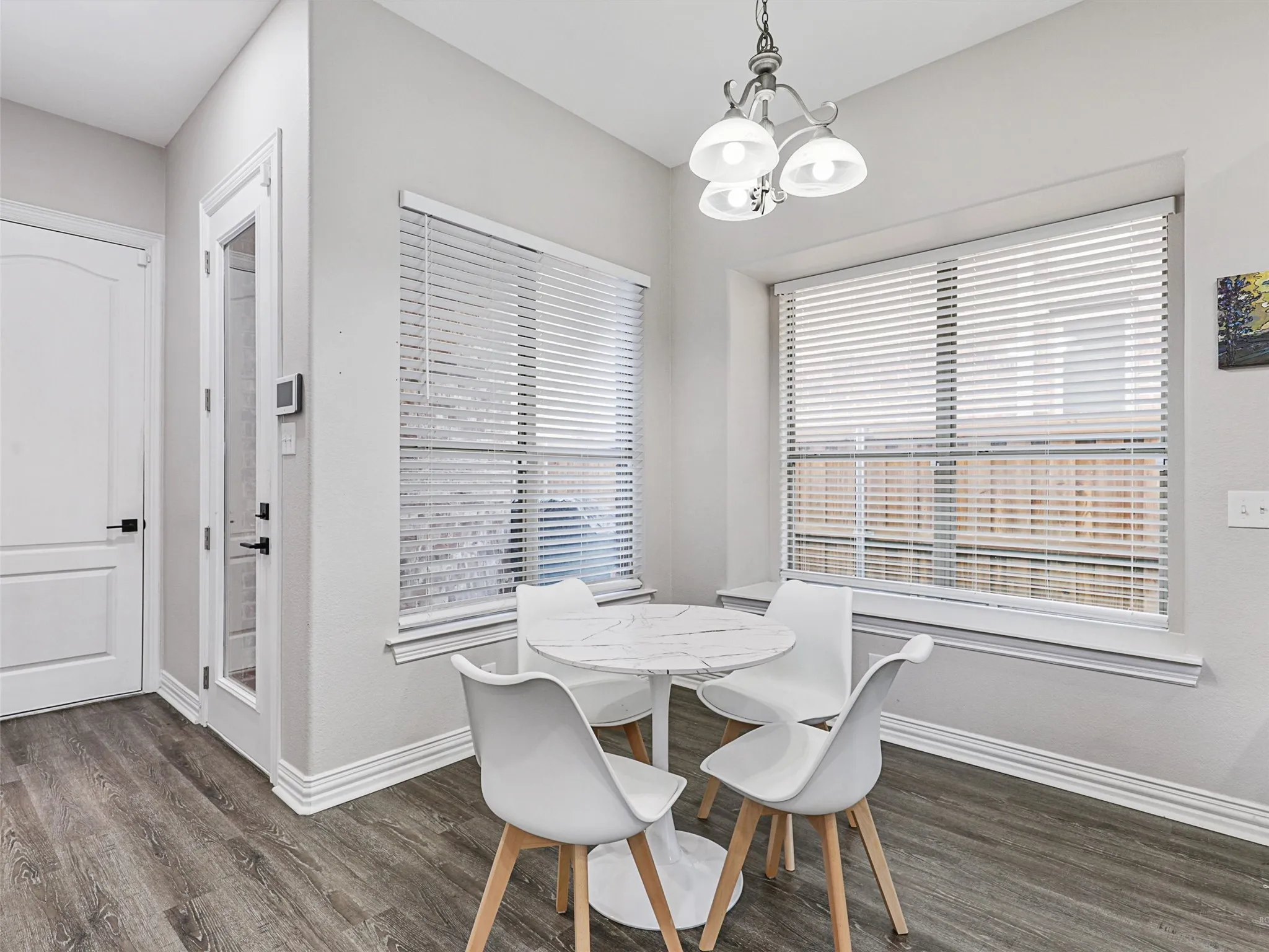 Dining nook featuring wood-finish flooring, a contemporary chandelier, two large windows with blinds, a white paneled door, and a glass-paneled exterior door