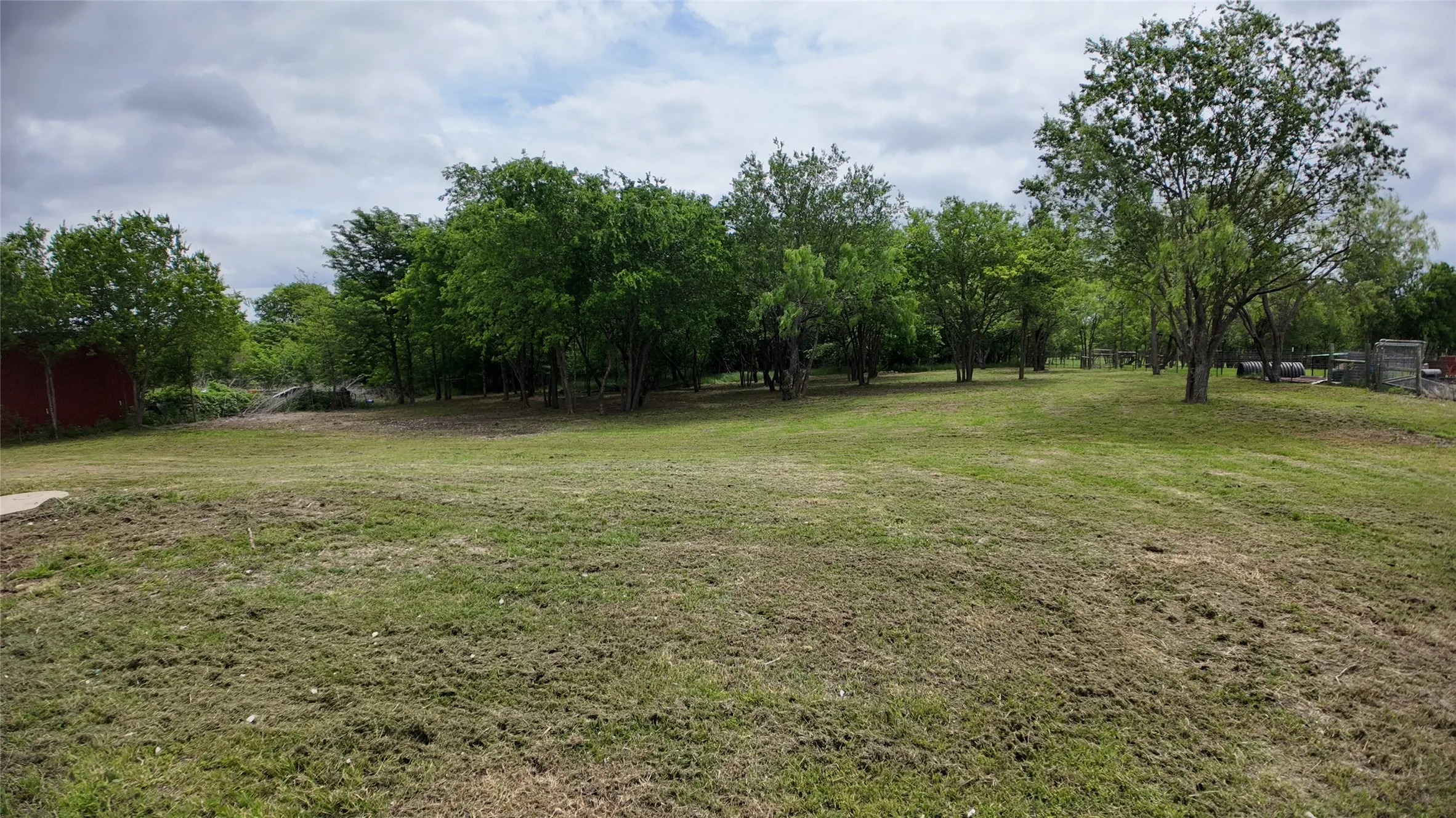 Expansive green space featuring scattered mature trees and additional dense tree coverage in the background