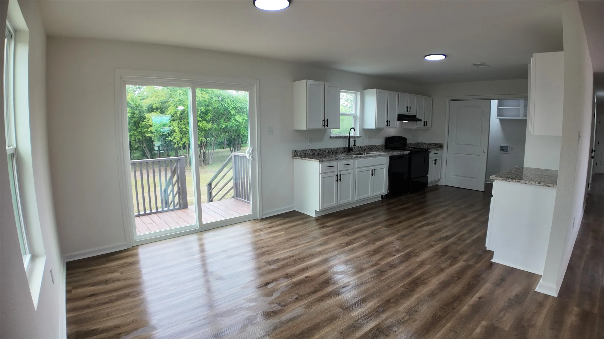 Open-concept interior featuring wood-finish flooring, white cabinetry, and granite-style countertops