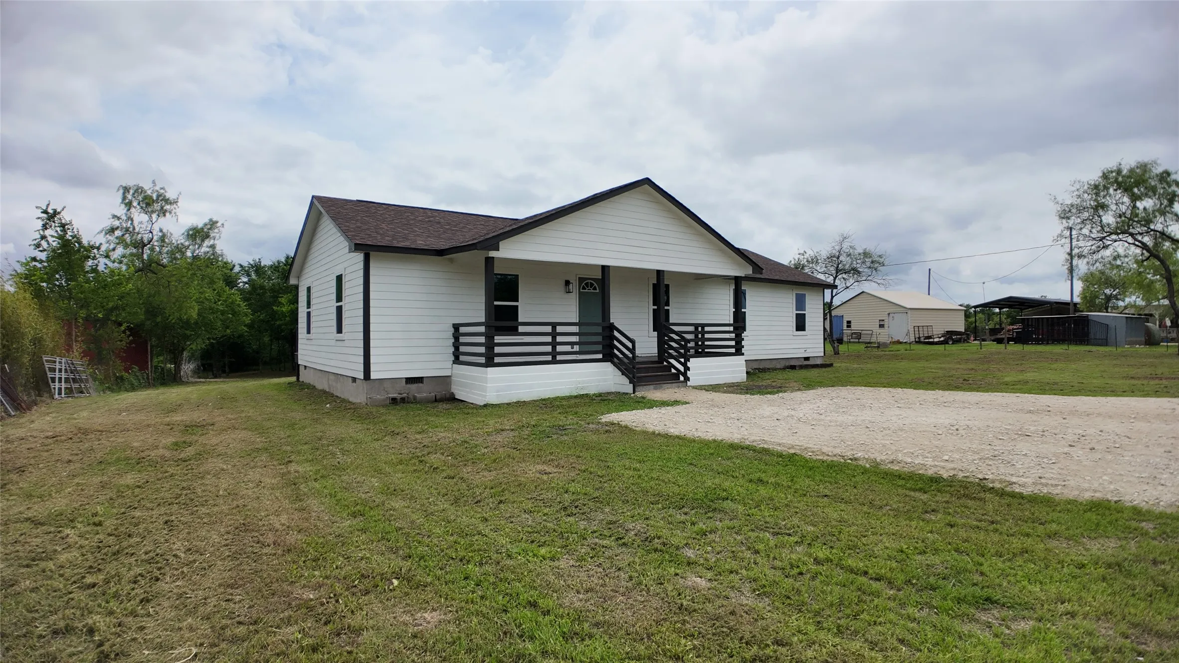 White siding exterior with dark trim and a covered front porch featuring black railings