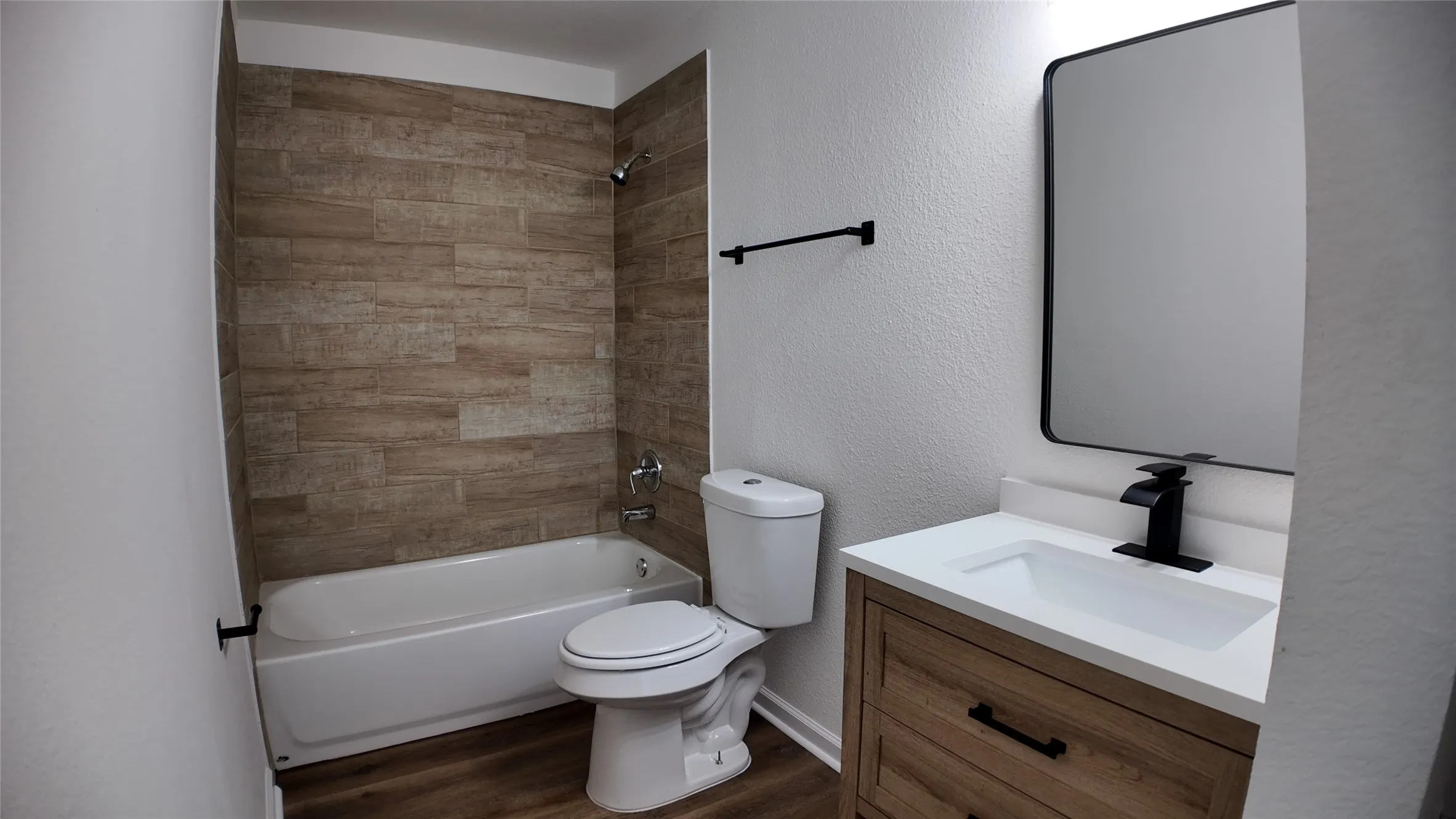 Bathroom featuring a tub/shower combination with wood-finish tile surround, a white toilet, and wood-finish vanity with a white countertop and rectangular sink
