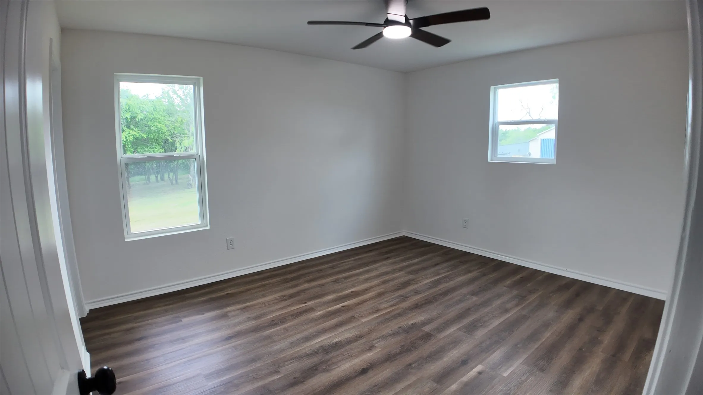 Spacious interior room featuring wood-finish flooring, a modern ceiling fan, and white baseboards