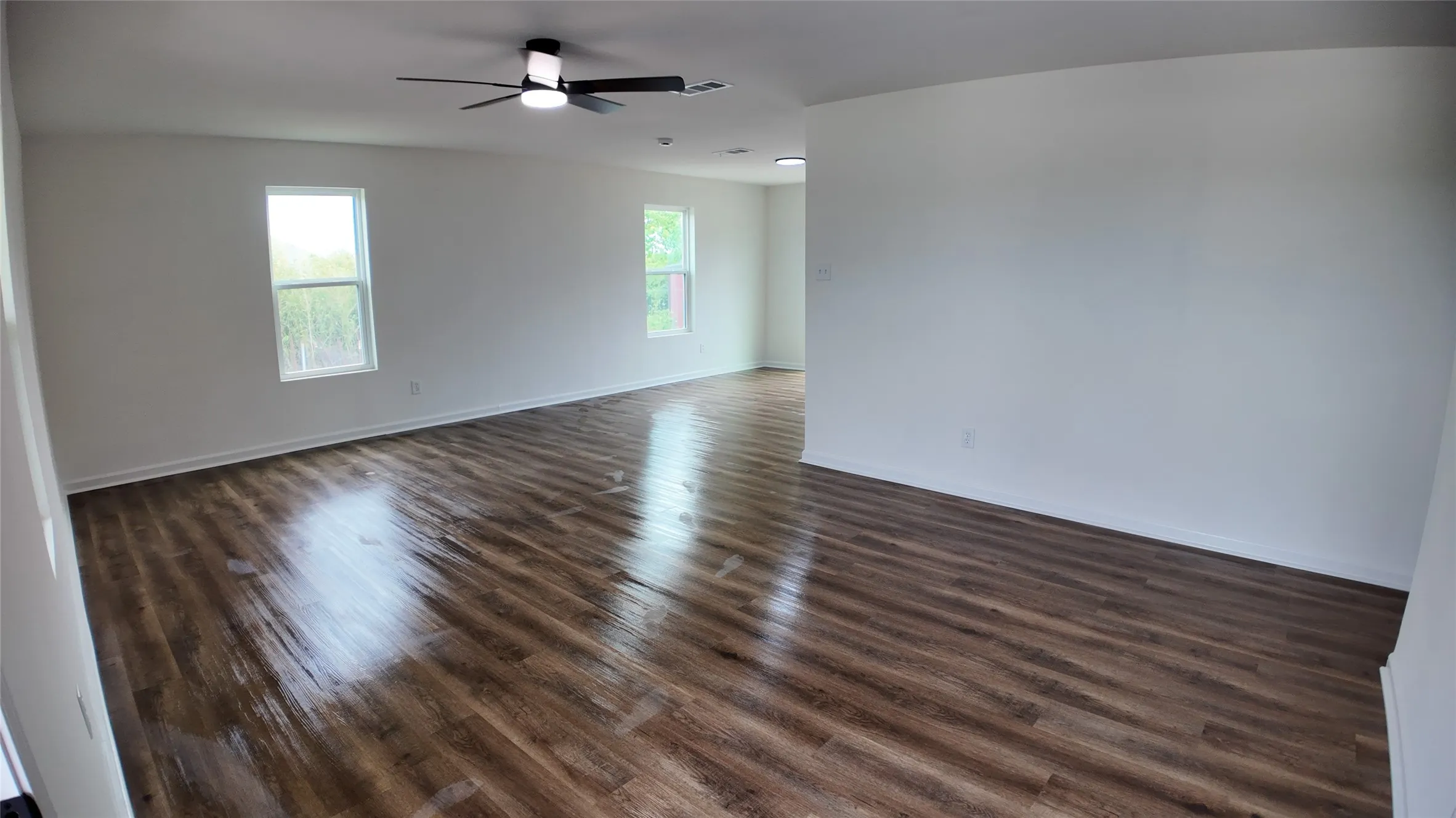 Spacious room featuring wood-finish flooring, white walls, and bright windows