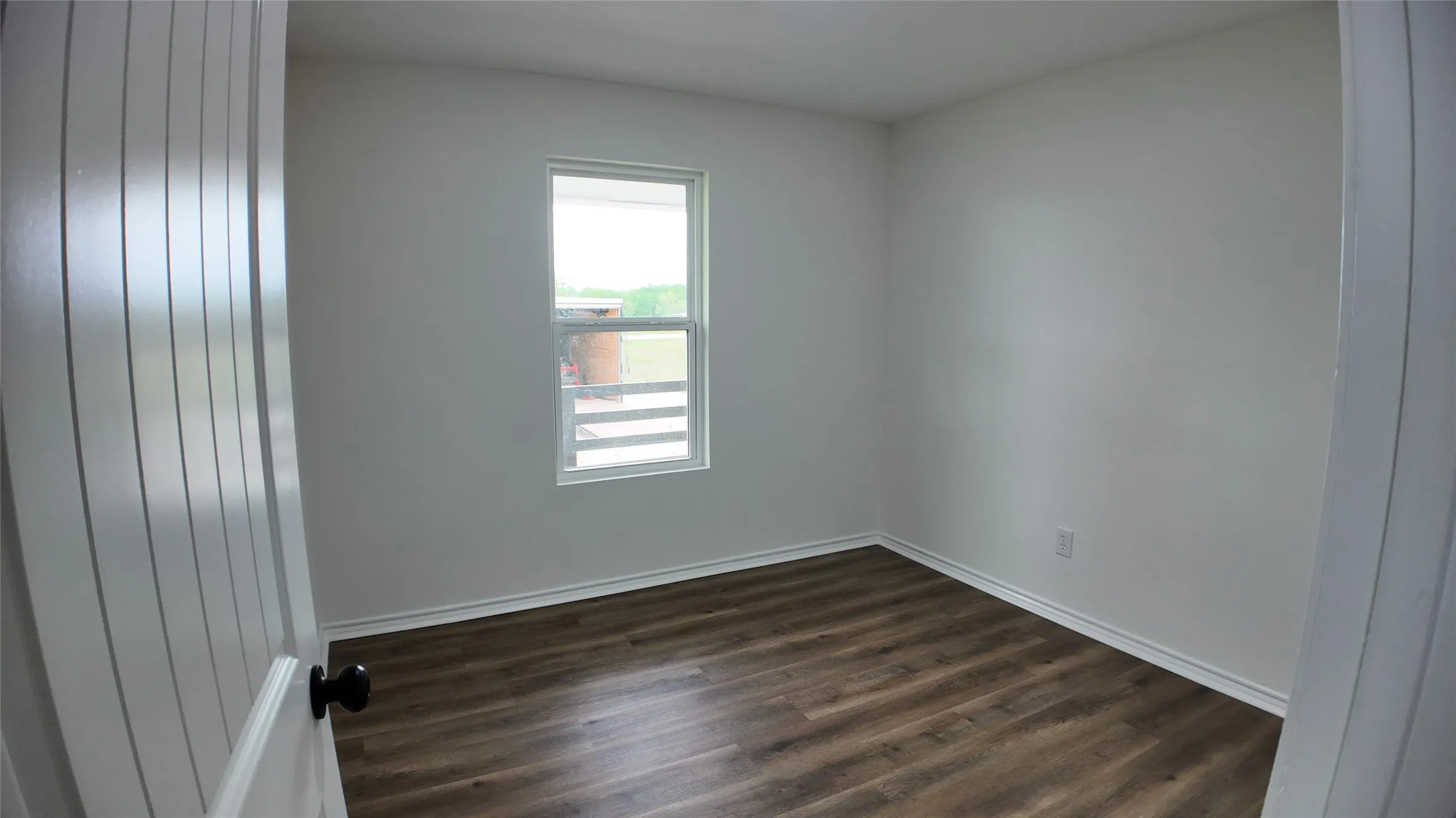 Bedroom featuring neutral wall paint, wood-finish flooring, white baseboards, and a single window