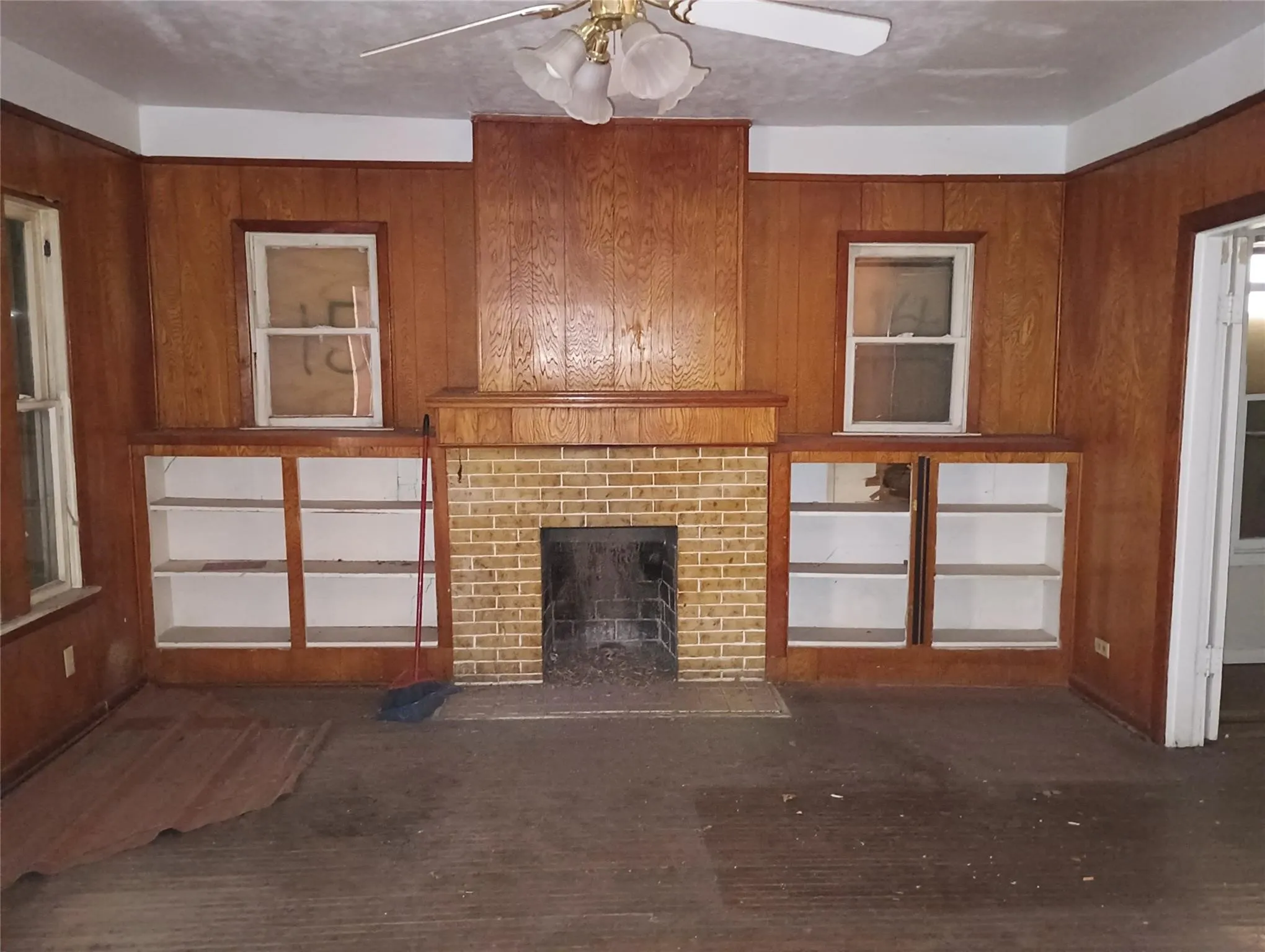 Room featuring wood paneling, a brick fireplace with a wood mantel, built-in shelving, and wood-finish flooring