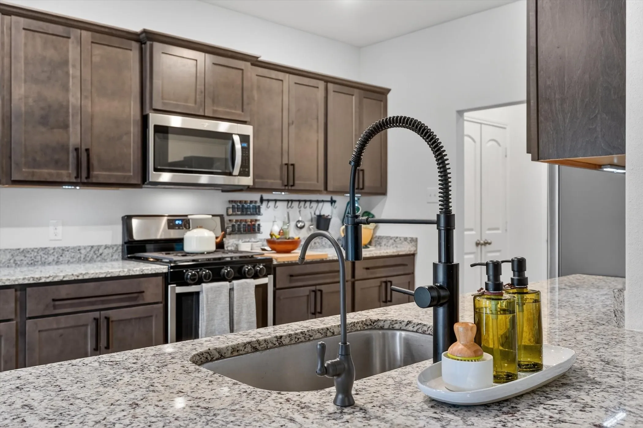 Kitchen featuring granite countertops, dark wood-finish cabinetry, stainless steel appliances, and a black gooseneck faucet with a single basin sink