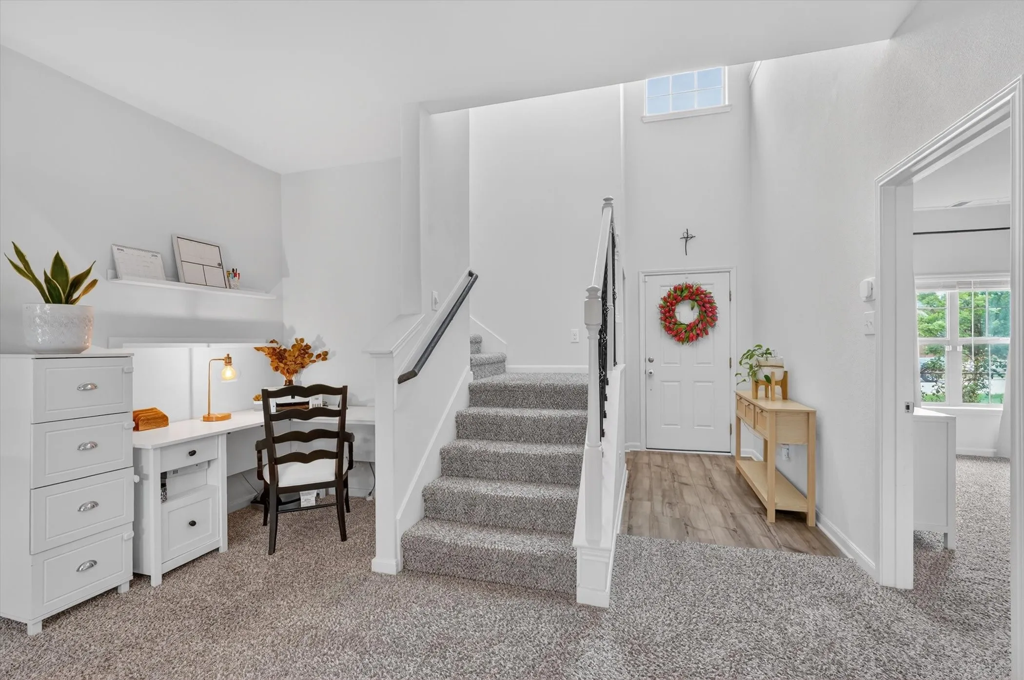 Light-filled entryway featuring high ceilings, wood-finish flooring, and a carpeted staircase with white risers and a black handrail