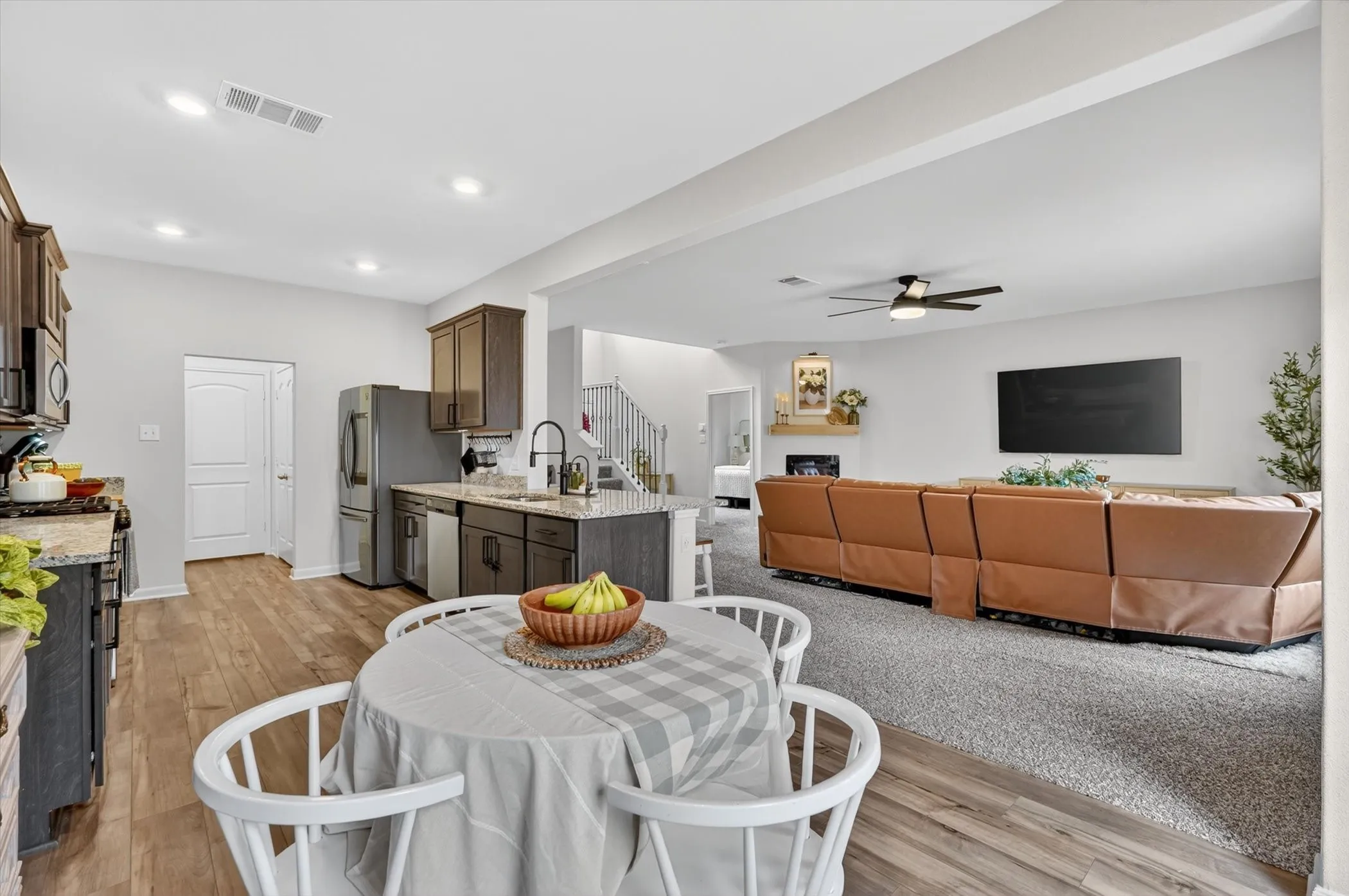 Open-concept living space featuring wood-finish flooring, a kitchen island with seating, dark wood cabinetry, a built-in fireplace with a mantel, and a ceiling fan