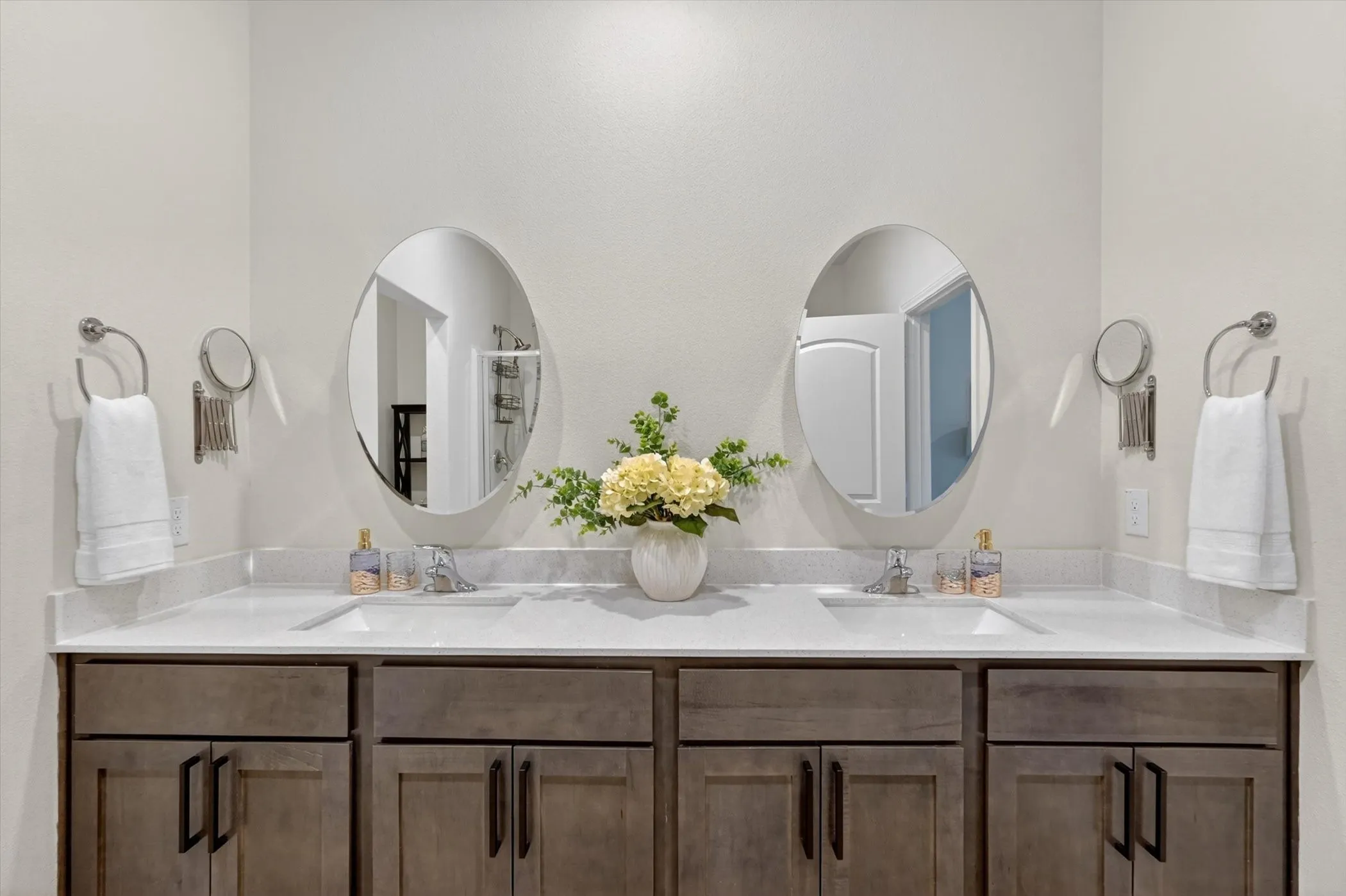 Double vanity with dual oval mirrors, white countertops, and wood-finish cabinetry