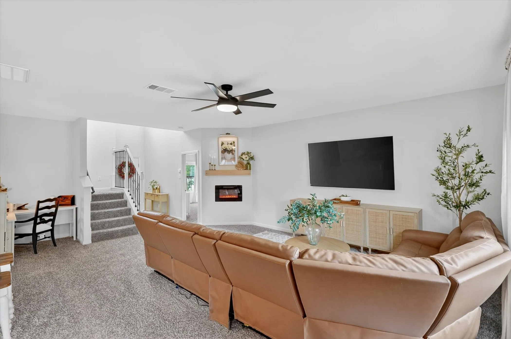 Spacious living area featuring a ceiling fan, plush carpet flooring, and a built-in fireplace with a light wood mantel