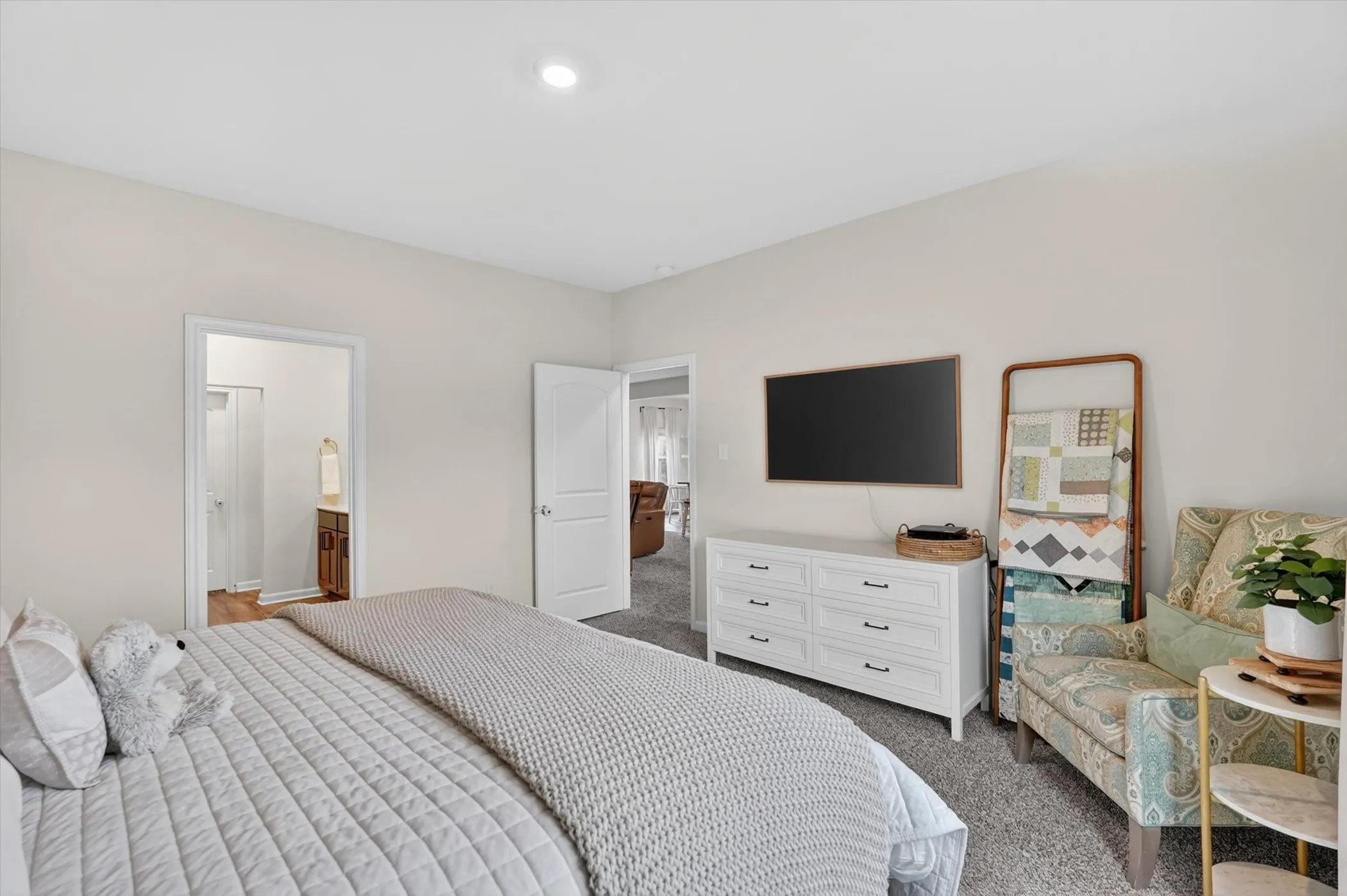 Carpeted bedroom featuring neutral wall tones, recessed lighting, a built-in television mount, and a doorway opening to a wood-finish flooring area