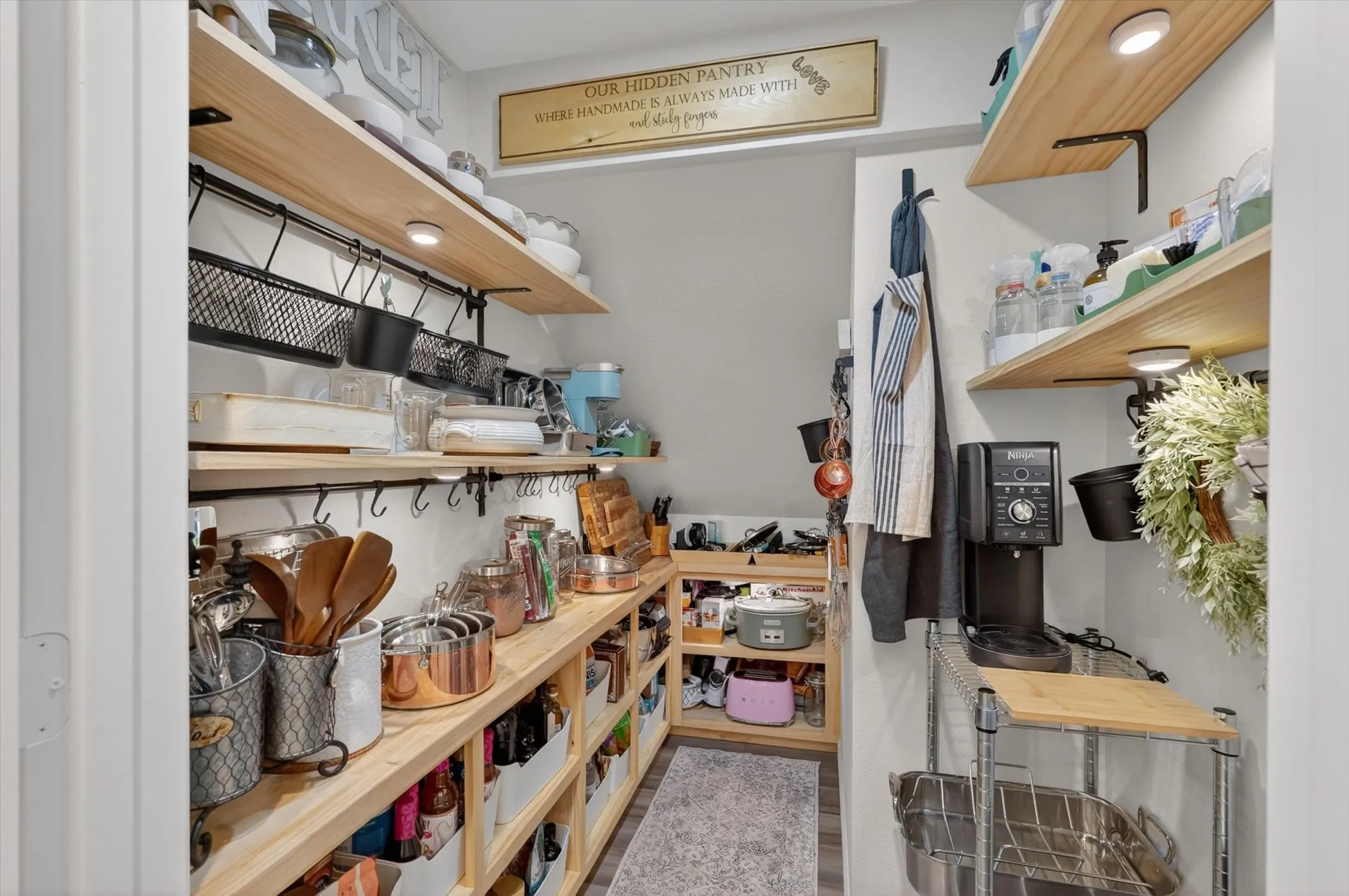 Organized pantry featuring multiple wood-finish shelves with under-shelf lighting, integrated hanging storage, and a built-in countertop area