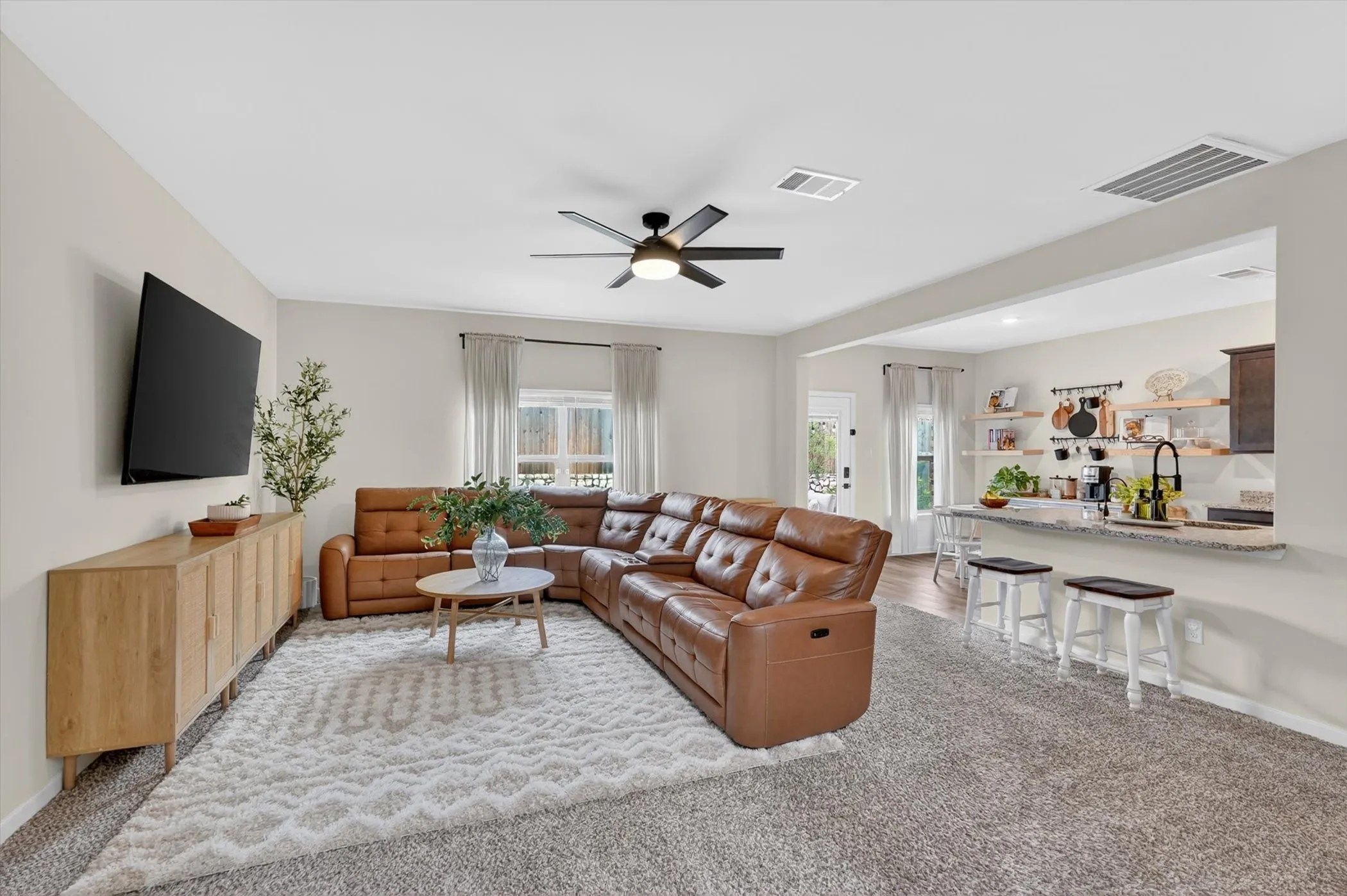 Open-concept living space featuring a ceiling fan, neutral wall paint, and a pass-through counter with a stone-finish surface