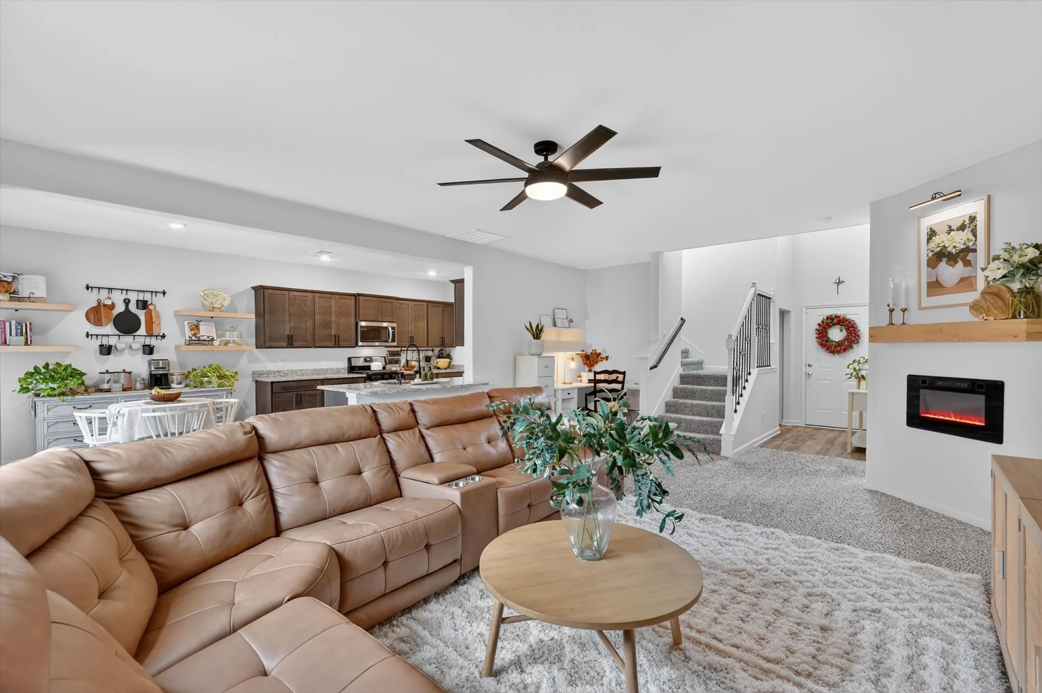 Spacious living area featuring a ceiling fan, plush carpeting, and an electric fireplace with a wood​​‌​​​​‌​​‌‌​‌‌​​​‌‌​‌​‌​‌​​​‌​​ mantle