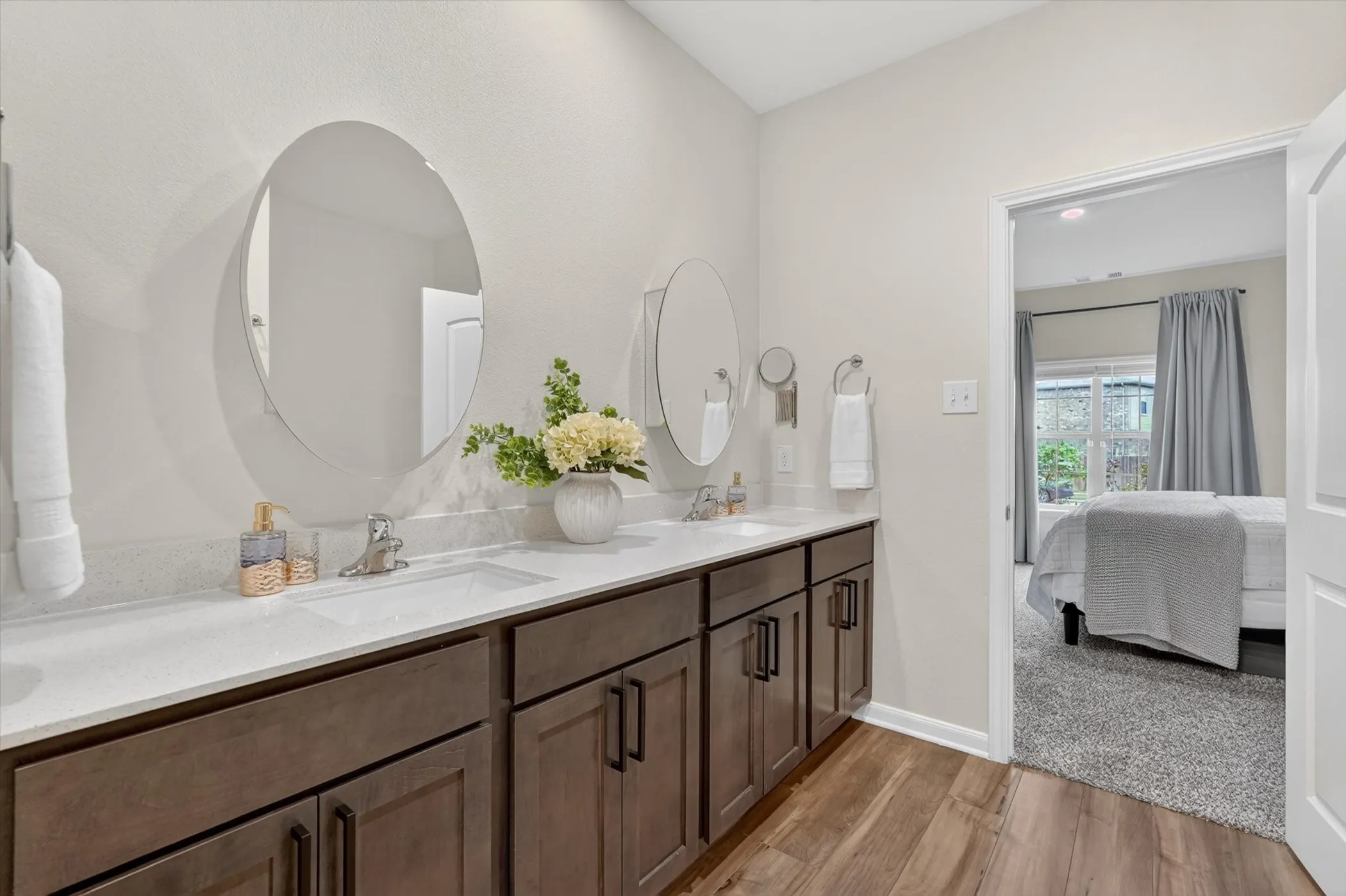 Double vanity with dark wood-finish cabinetry, white countertops, and modern circular mirrors