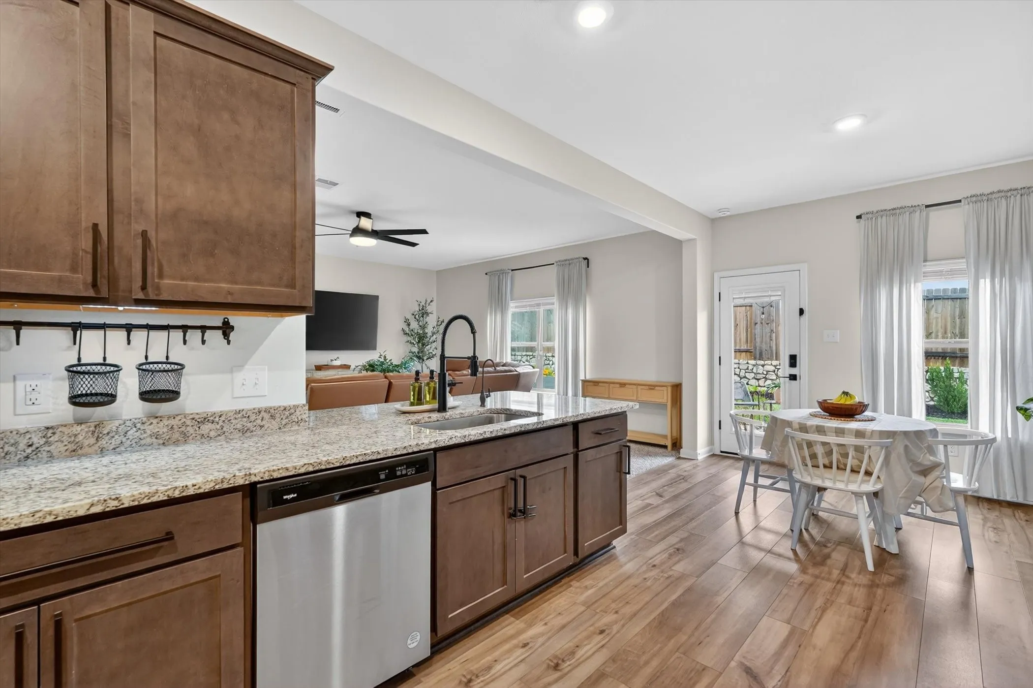 Kitchen island featuring a stainless steel sink with a black gooseneck faucet, light granite countertops, dark wood-finish cabinetry, and a built-in stainless steel dishwasher