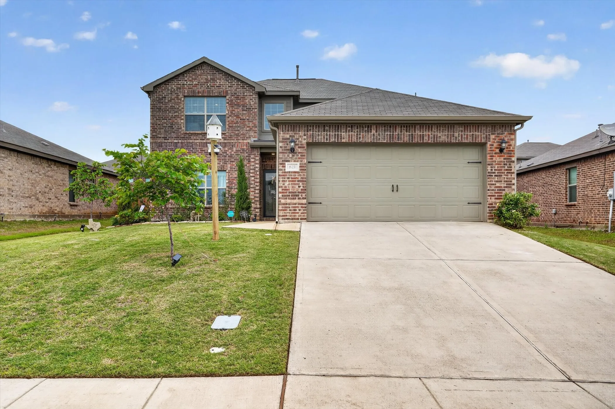 Brick exterior featuring a two-car garage, concrete driveway, and front lawn