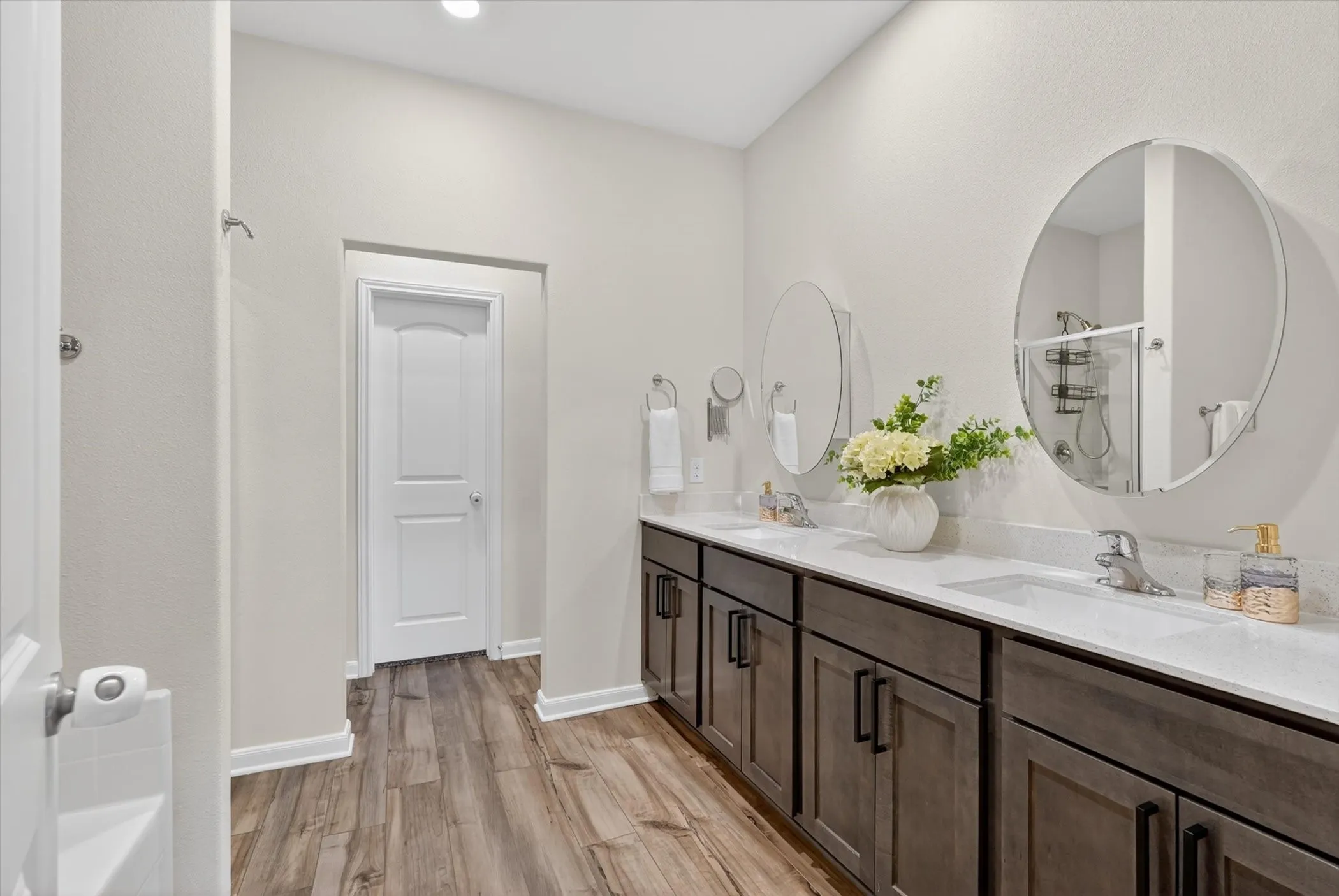 Dual vanity with undermount sinks, wood-finish flooring, white countertops, and circular mirrors