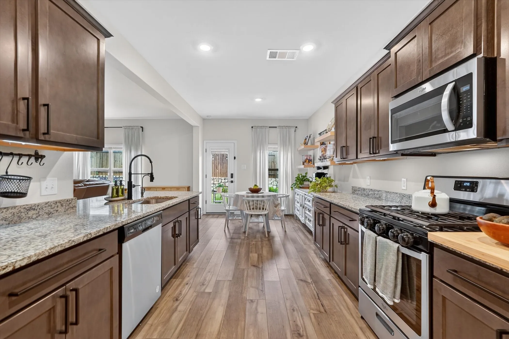 Open-concept kitchen featuring wood-finish flooring, dark wood cabinetry with black hardware, light-colored countertops, stainless steel appliances, and recessed lighting