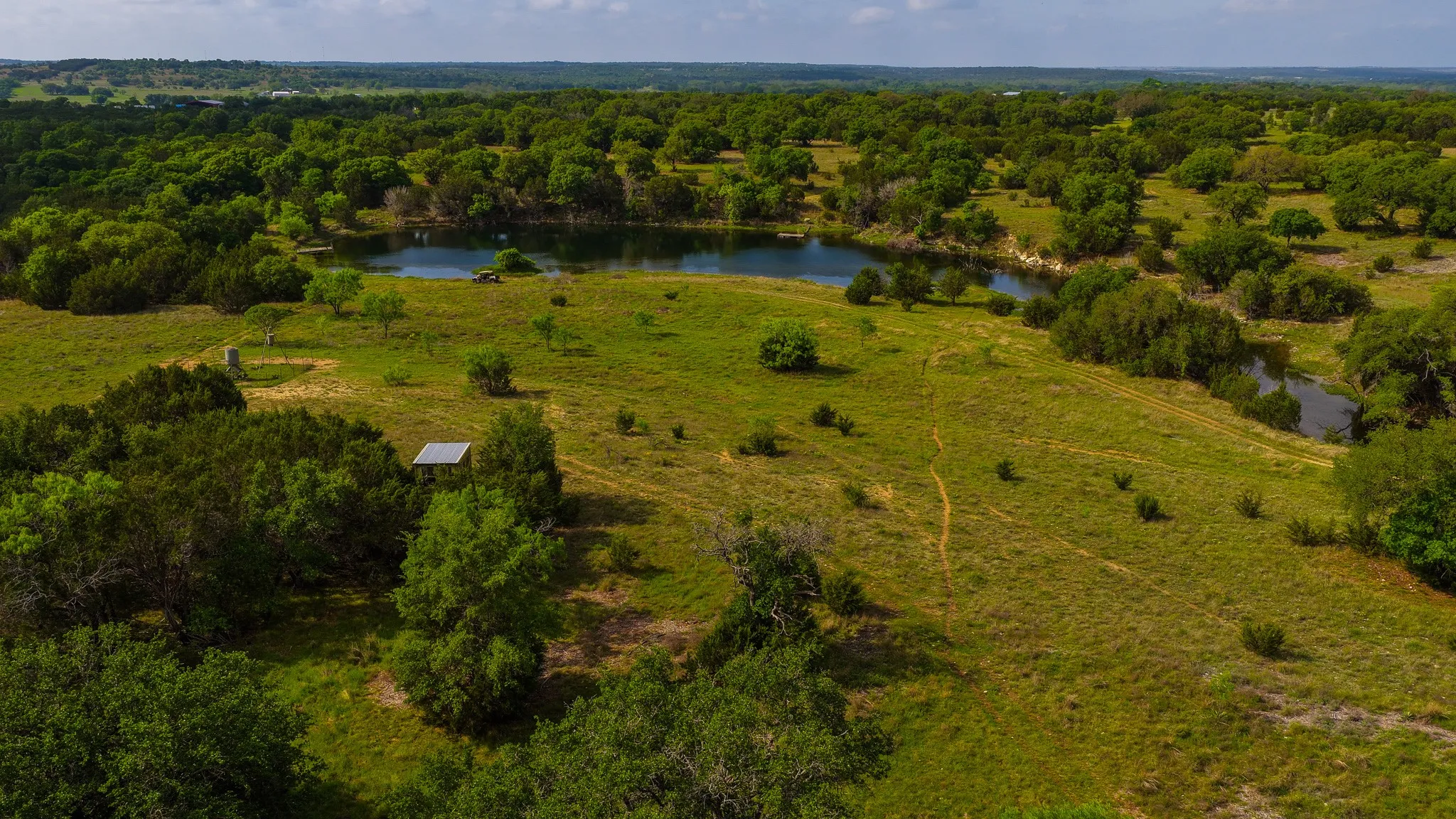 Expansive acreage featuring a central pond, rolling green terrain, and abundant mature trees