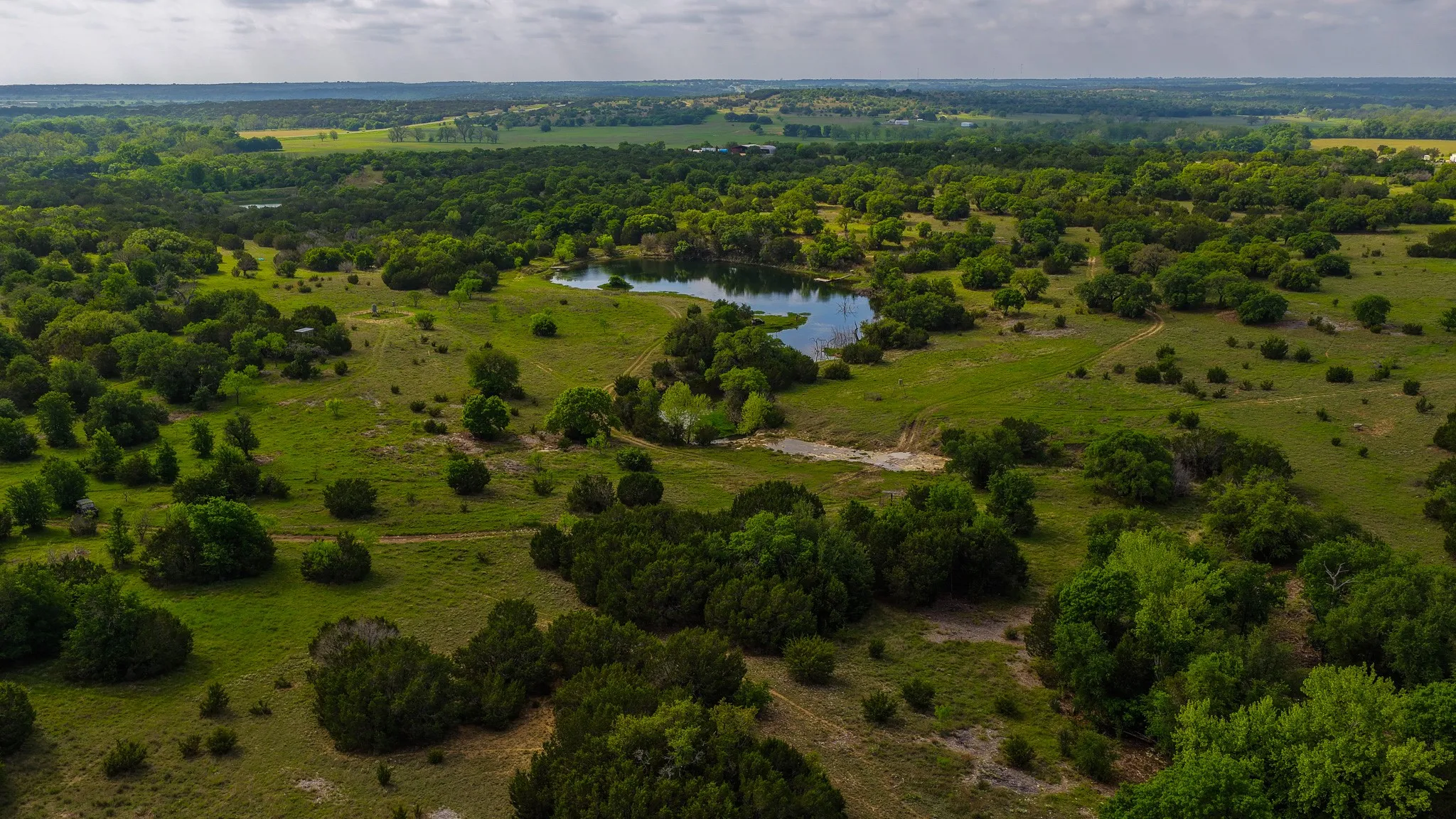 Expansive acreage featuring a natural pond, verdant grasslands, scattered trees, and distant rolling terrain