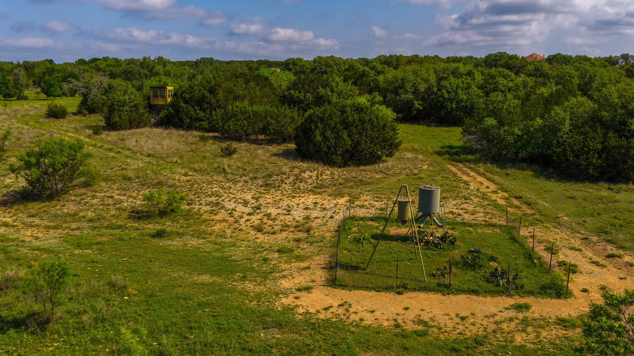 Expansive land featuring a water storage tank, pump system, dense tree coverage, and a distant elevated structure