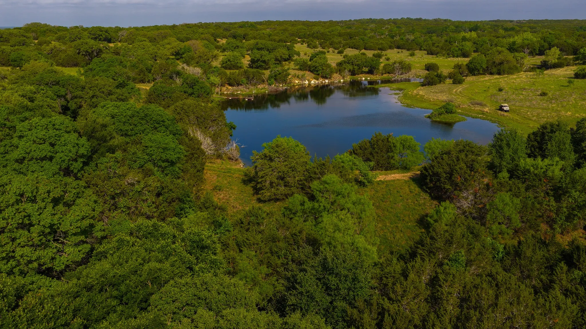 Natural landscape featuring a private pond surrounded by mature trees and open grassy areas