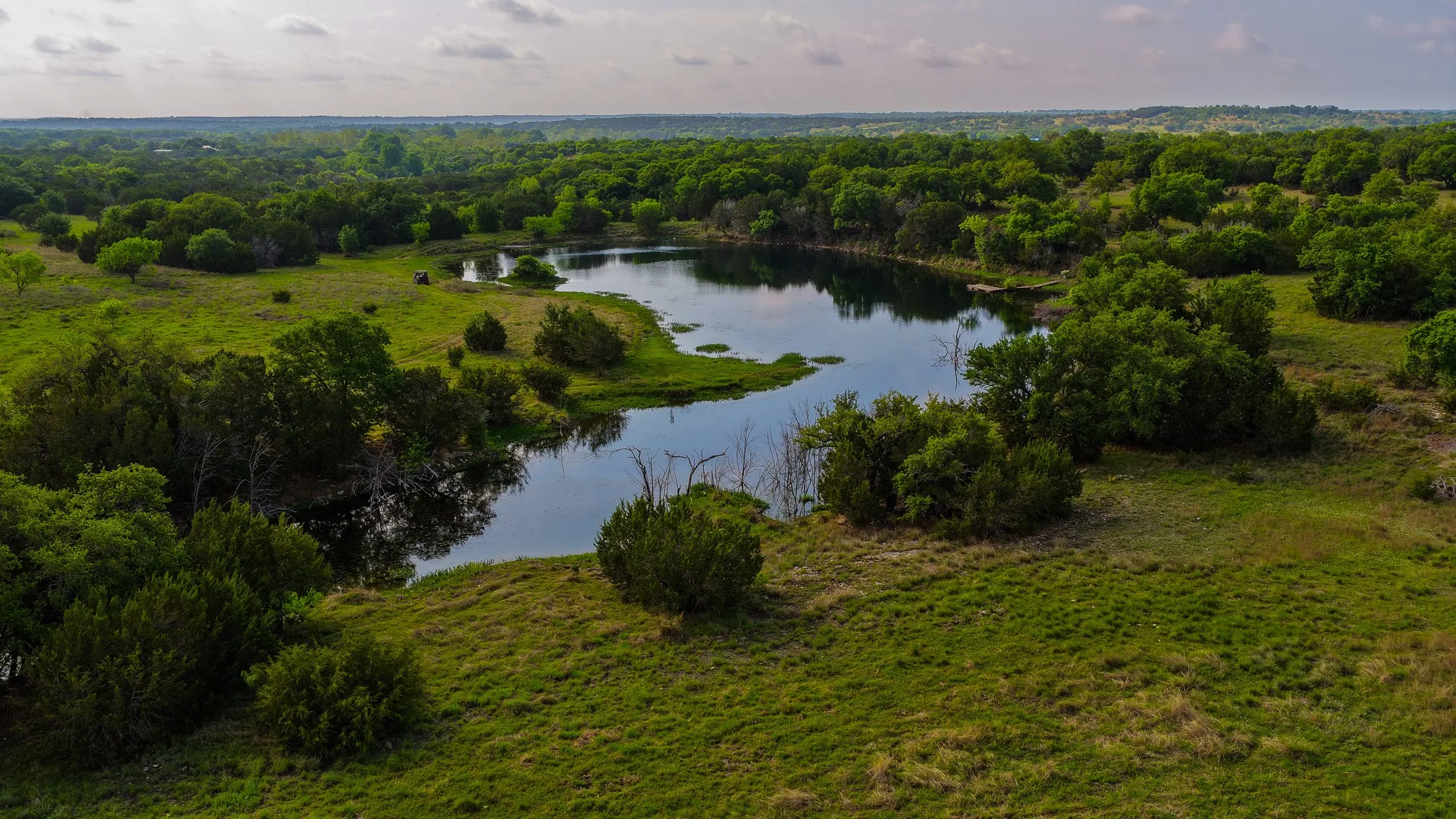 Natural landscape featuring a tranquil body of water, surrounded by lush green foliage and mature trees