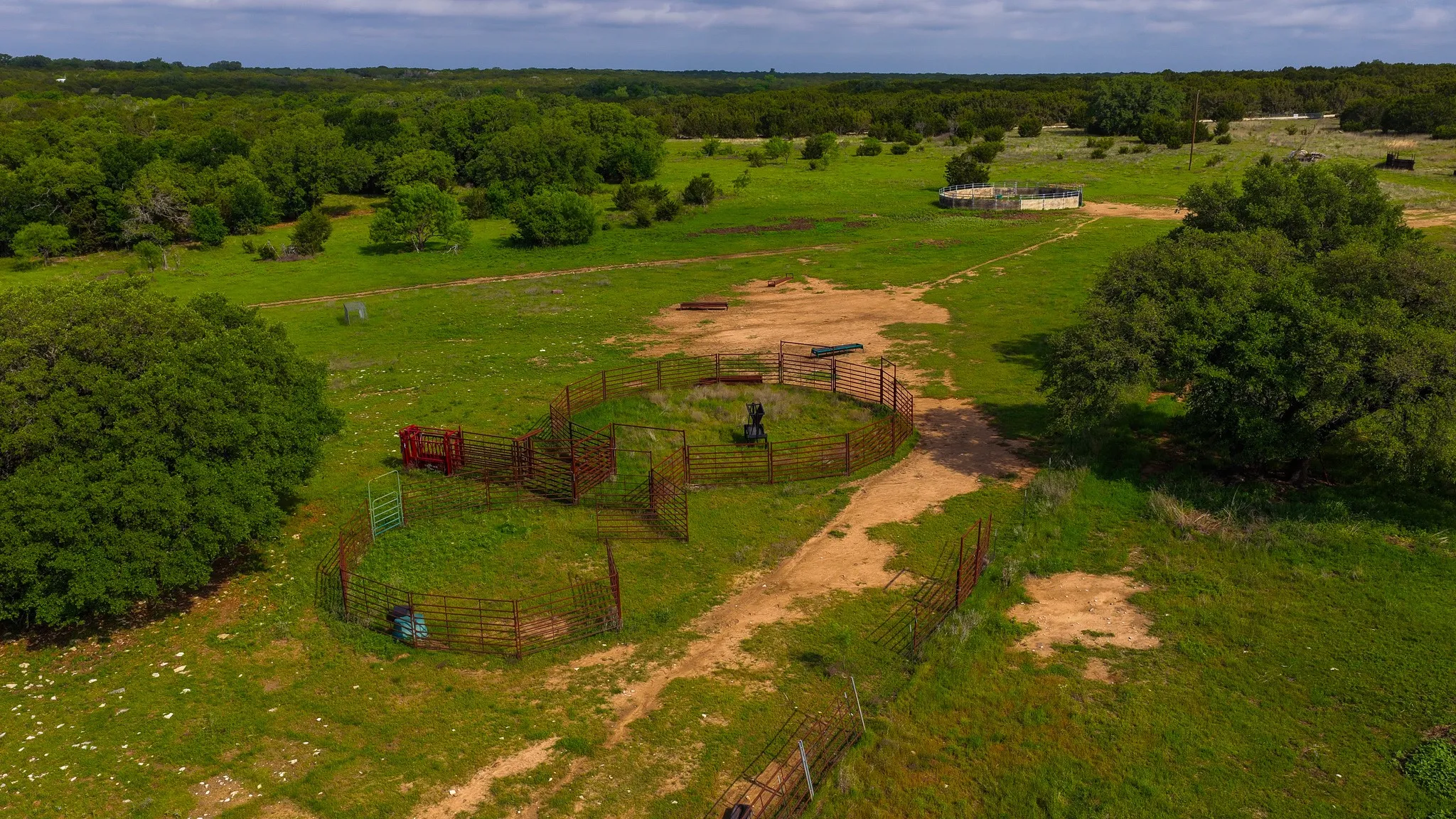 Expansive green acreage featuring a circular metal pen, additional metal fencing, and mature trees