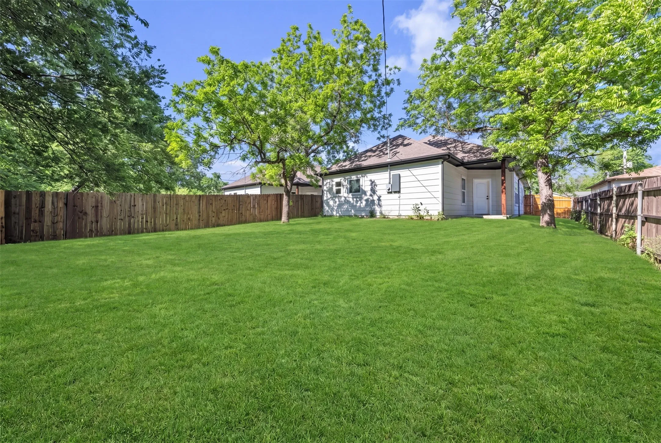 Expansive rear yard featuring a large grass area, mature trees, and a privacy fence