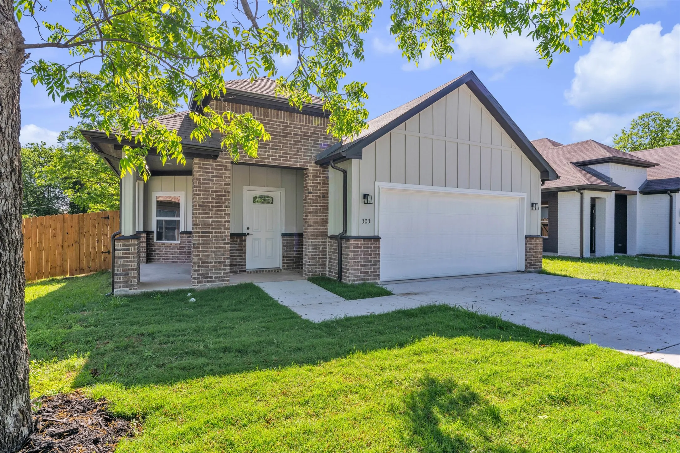 Contemporary residence featuring a brick and board-and-batten facade, covered front porch, attached garage, concrete driveway, and manicured lawn