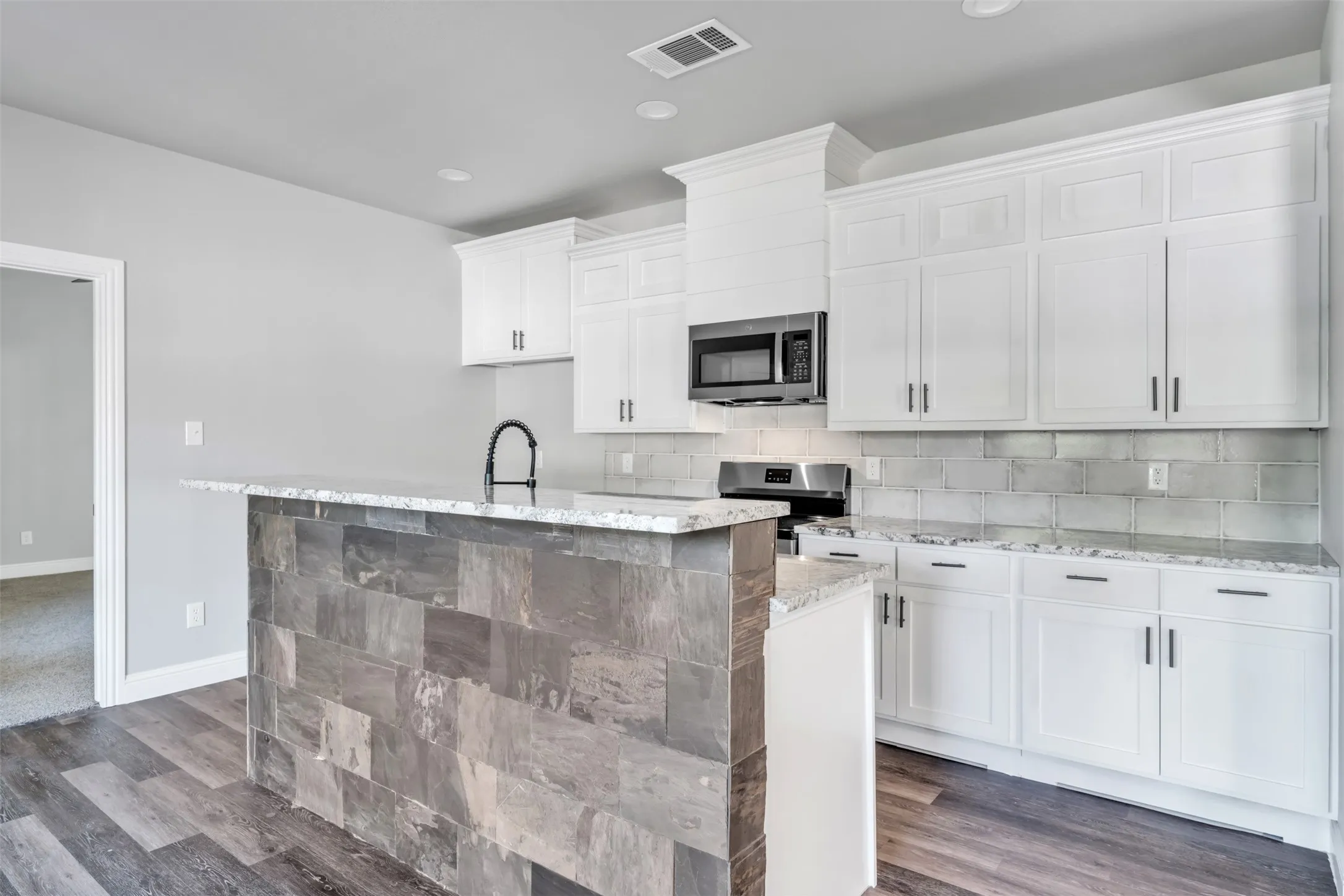 Kitchen featuring a tiled island, granite countertops, white cabinetry with dark hardware, a stainless steel microwave, and wood-finish flooring
