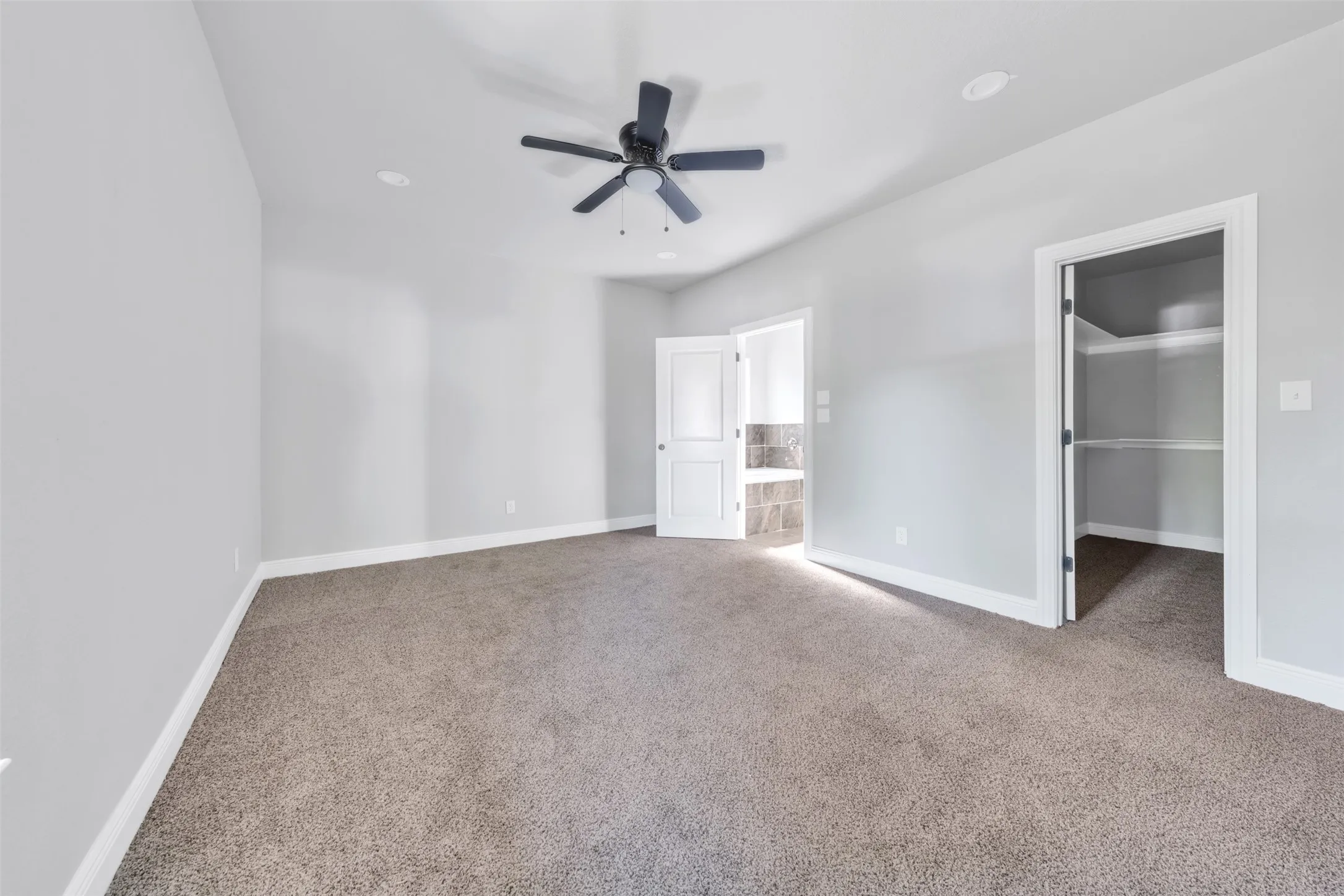 Spacious room featuring neutral carpeting, light gray walls, a ceiling fan, recessed lighting, and a walk-in closet with built-in shelving