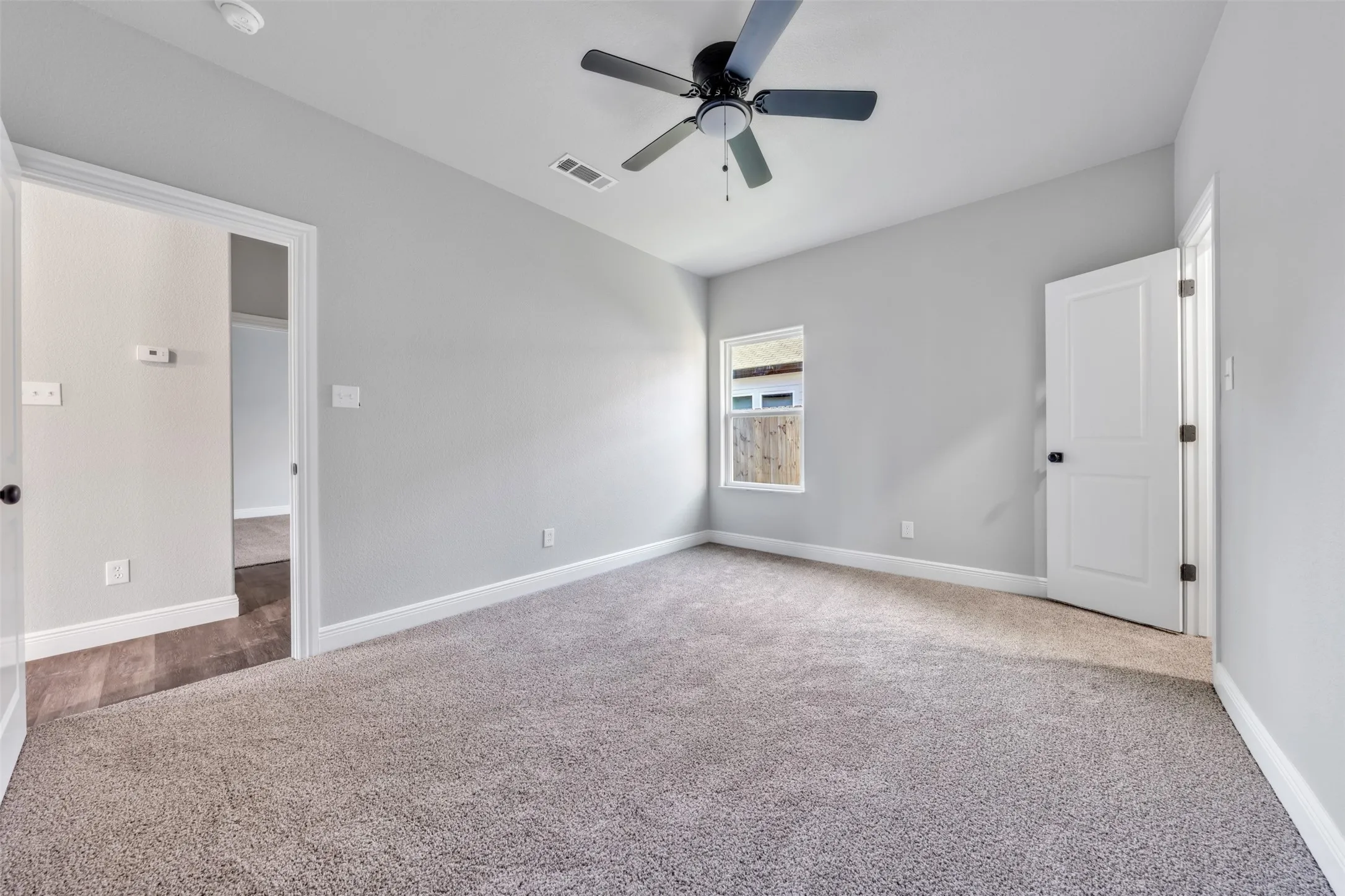 Carpeted interior room featuring light gray walls, white trim, a ceiling fan, and a single window