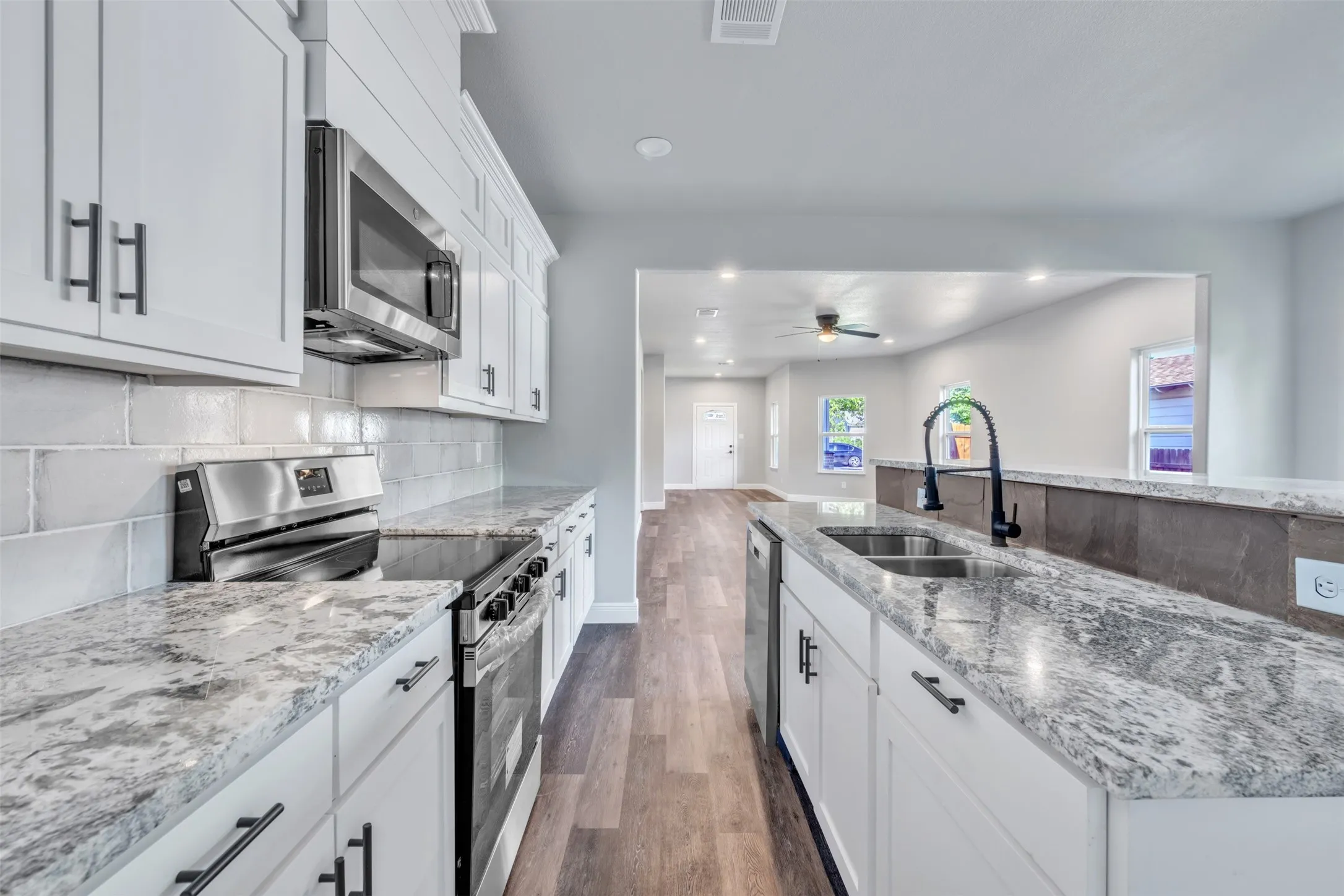 Modern kitchen featuring white cabinetry, stone-finish countertops, stainless steel appliances, and wood-finish flooring