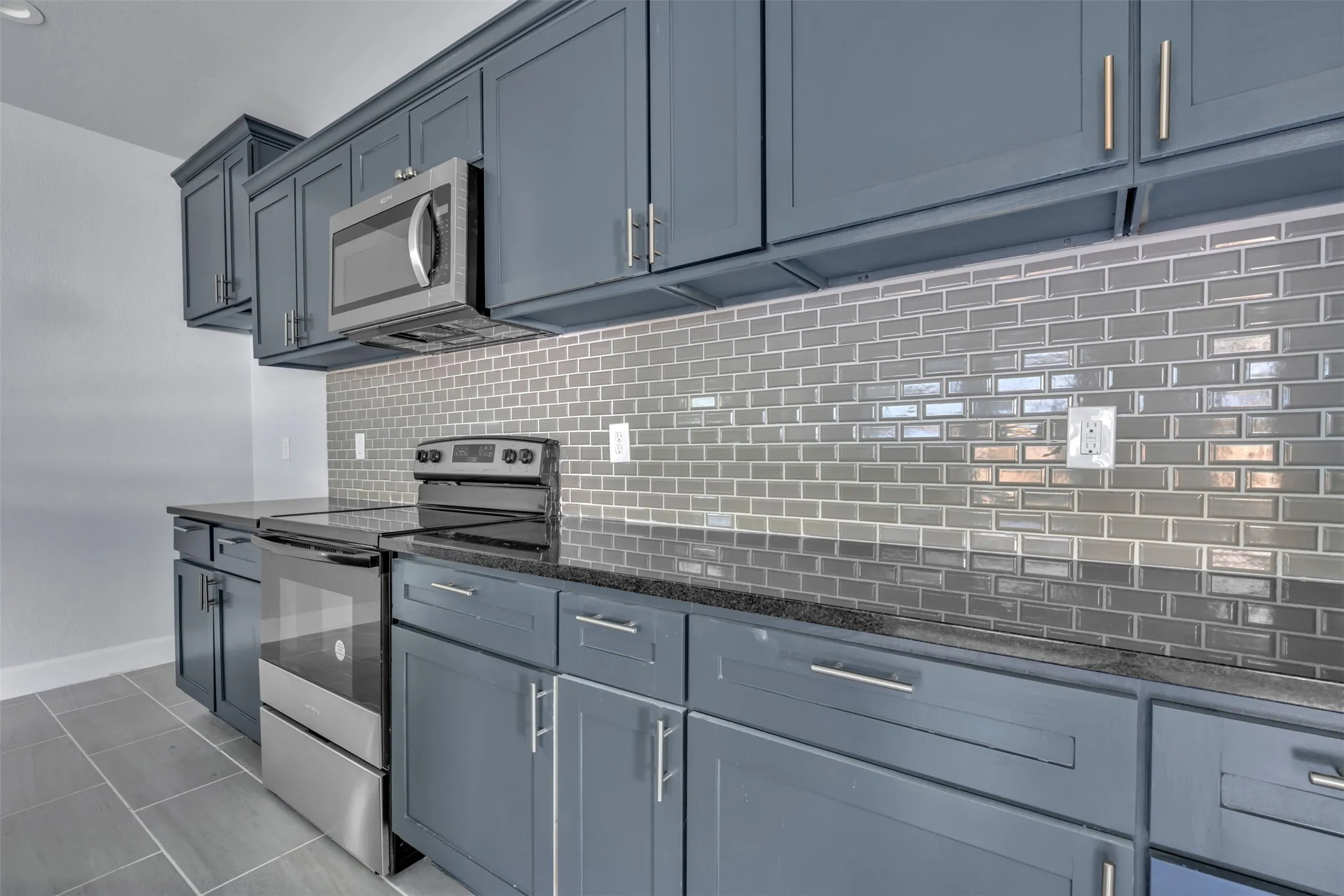 Kitchen featuring dark cabinetry, dark countertops, a glass subway tile backsplash, stainless steel appliances, and tile flooring