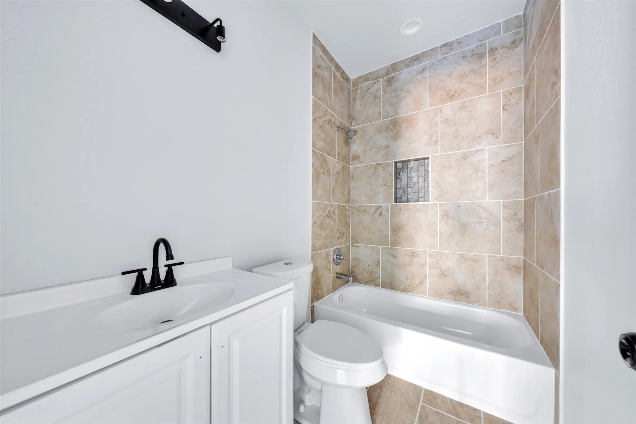 Bathroom featuring a white vanity with integrated sink, matte black faucet, and a tiled tub/shower combination