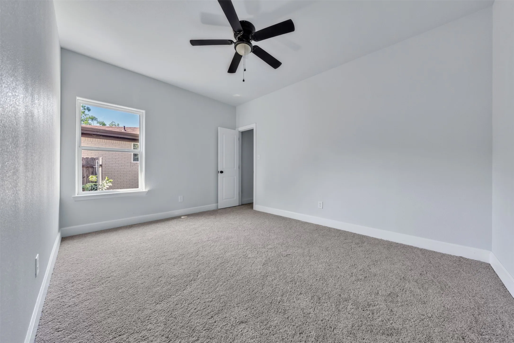Carpeted room featuring a single window with white trim, a black ceiling fan, and white baseboards
