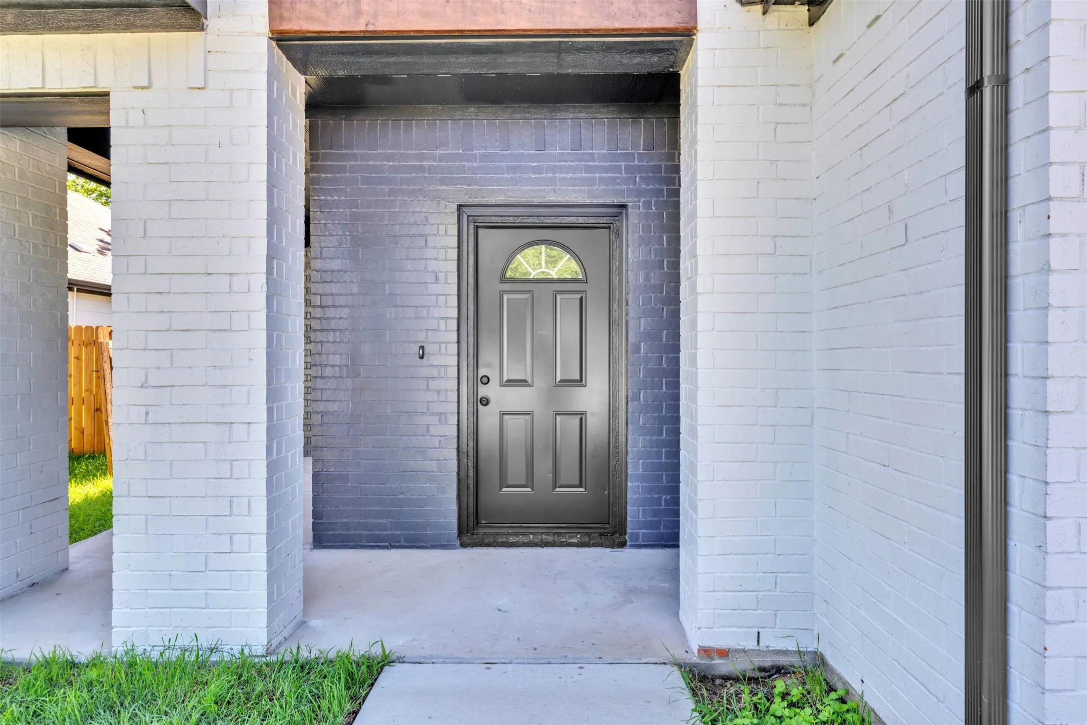 Entryway featuring a dark gray door with an arched window insert, set against a dark brick accent wall