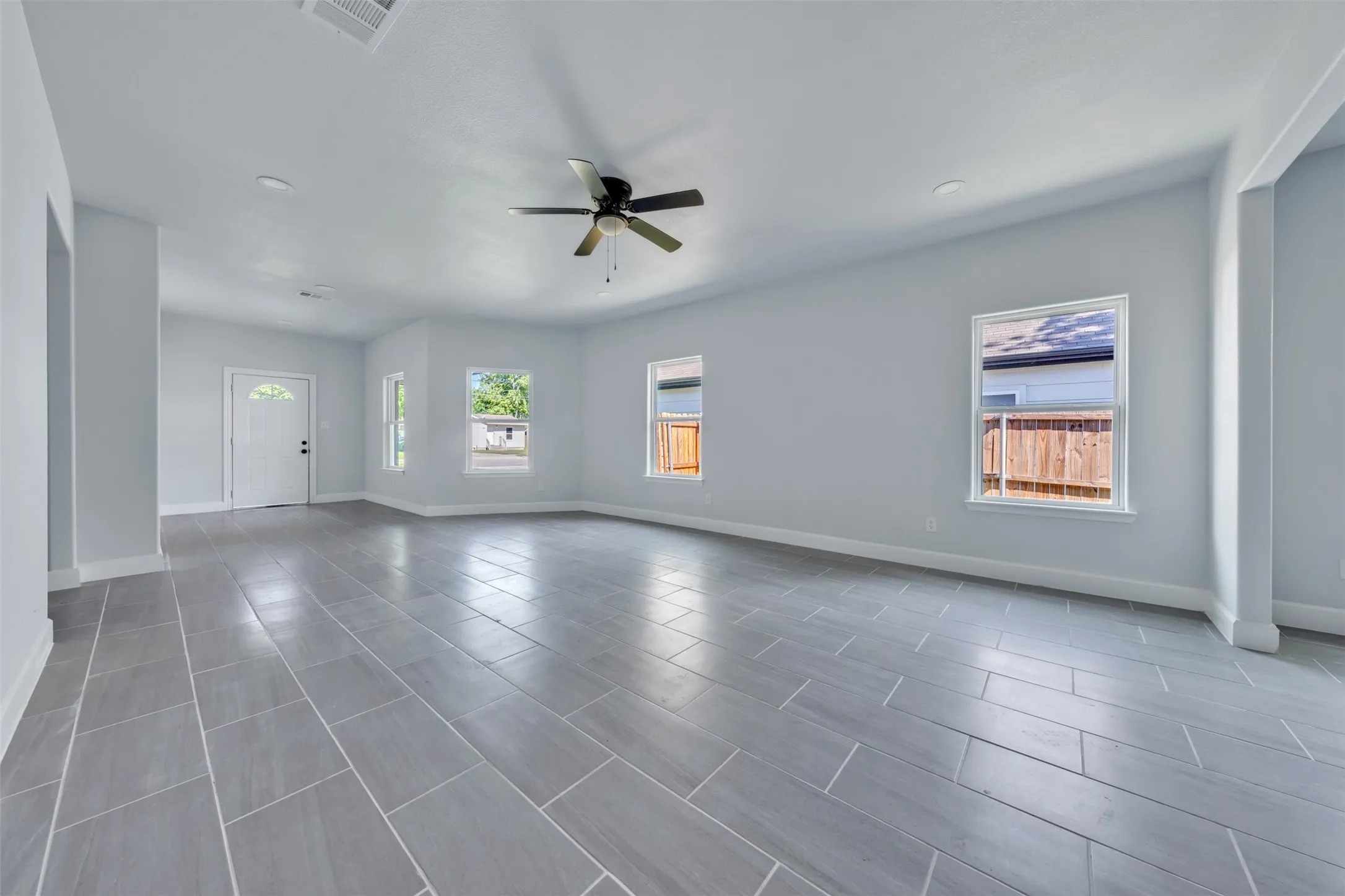 Spacious interior featuring large format tile flooring, a ceiling fan, recessed lighting, multiple windows, and a white entry door with an arched glass insert