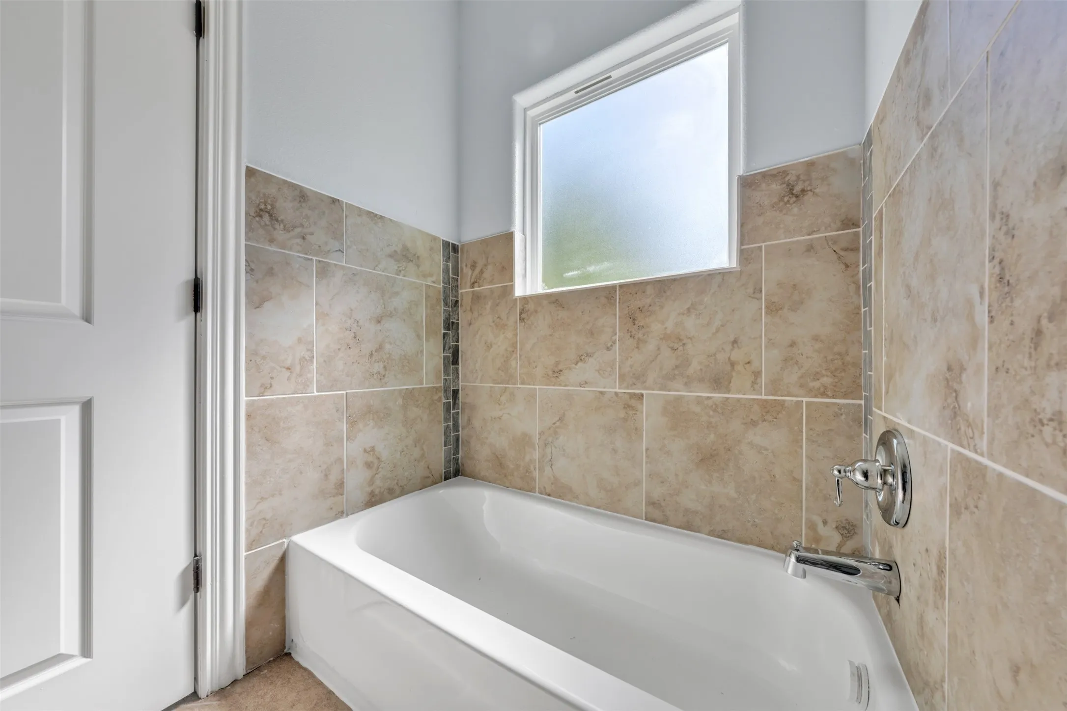 Bathtub featuring a tiled surround, decorative mosaic accent, chrome fixtures, and a frosted window
