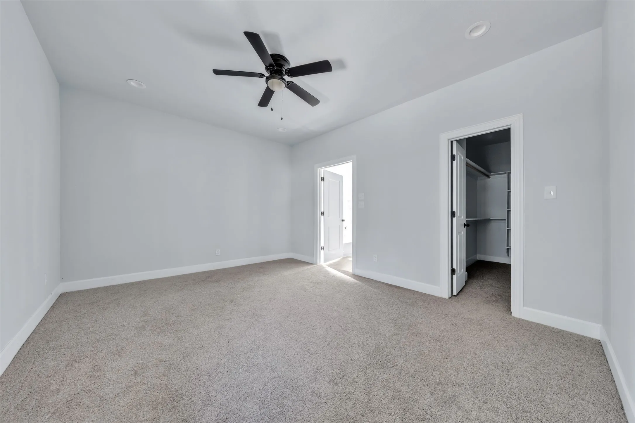 Spacious room featuring neutral carpet flooring, light gray wall paint, a black ceiling fan, and recessed lighting